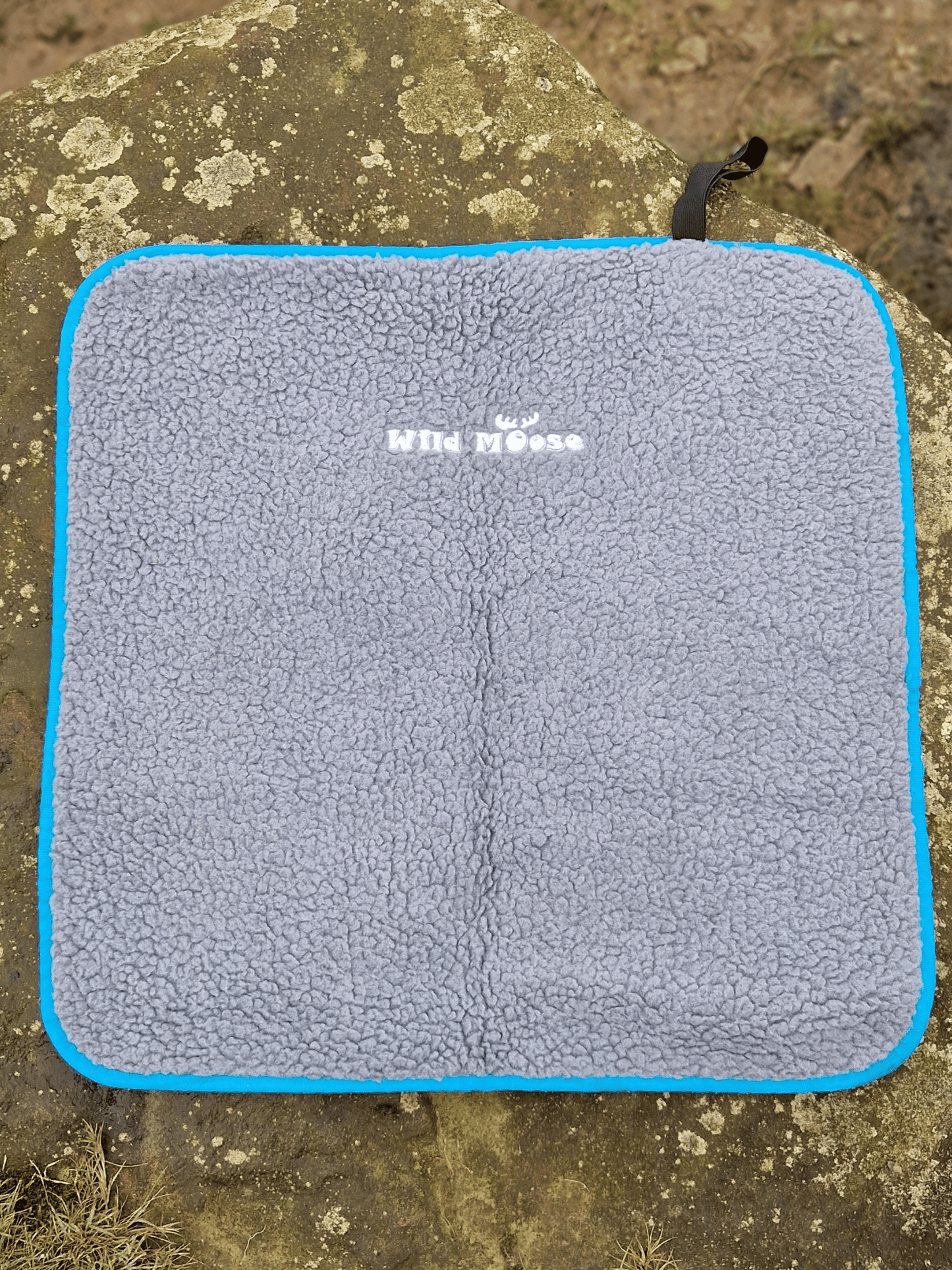 a fleece lined changing mat on a rock showing the logo Wild Moose and the elastic binding strap