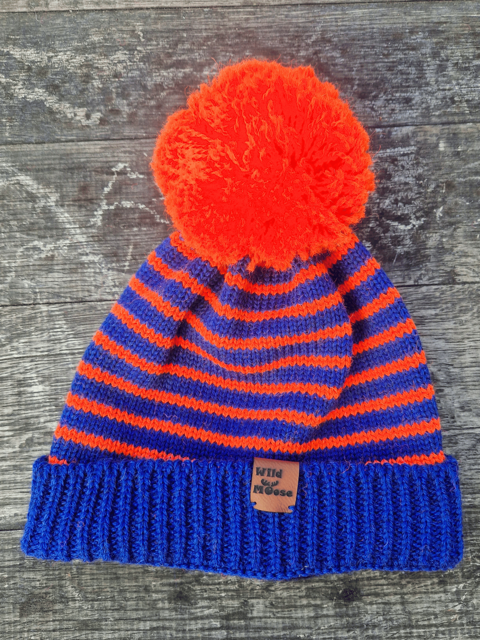 bobble hat in dark blue and vibrant orange stripes with orange pom displayed on a wooden surface.