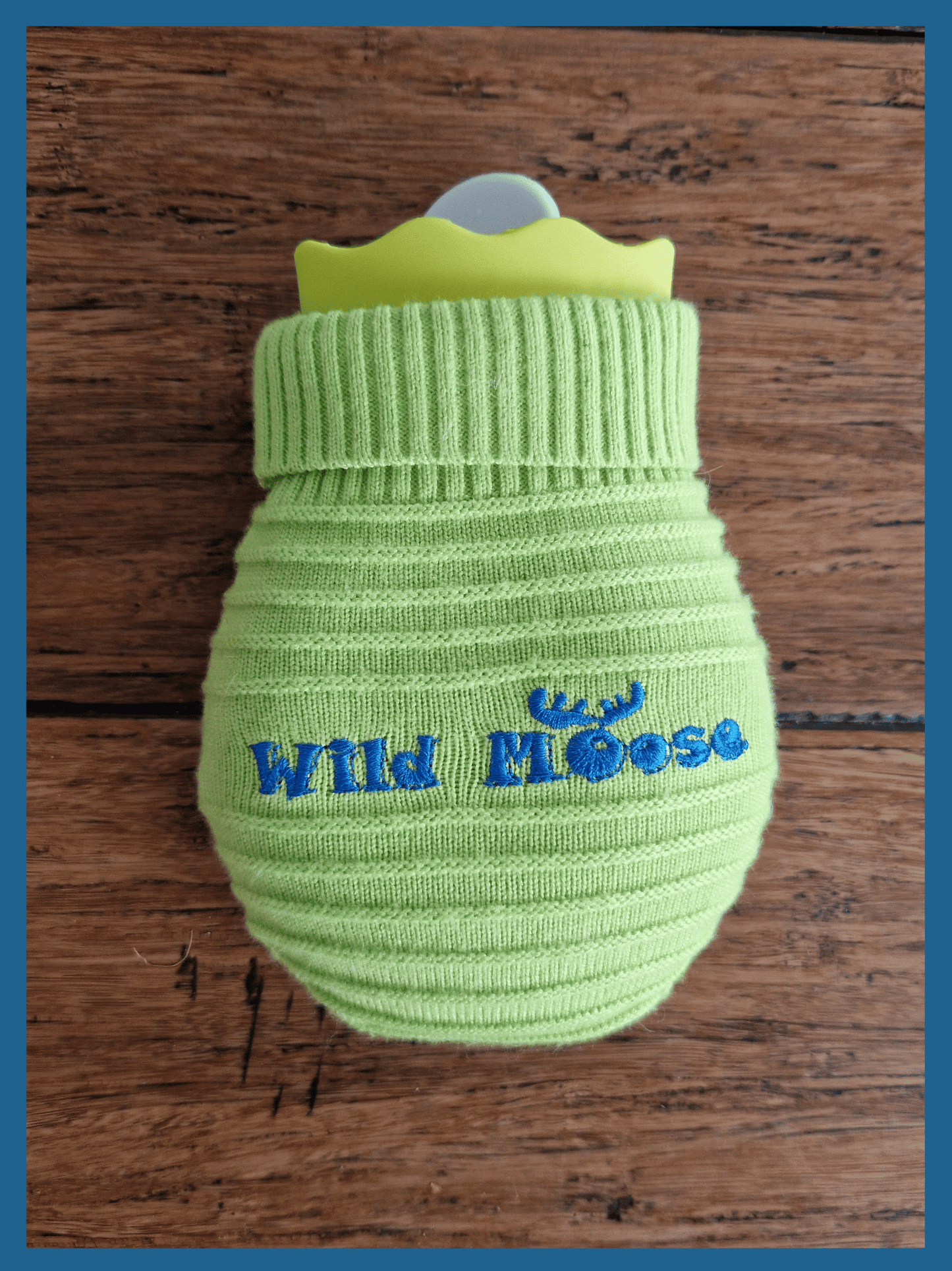 brightly coloured mini hot water bottle in a knitted cover in lime green against a wooden floor backdrop