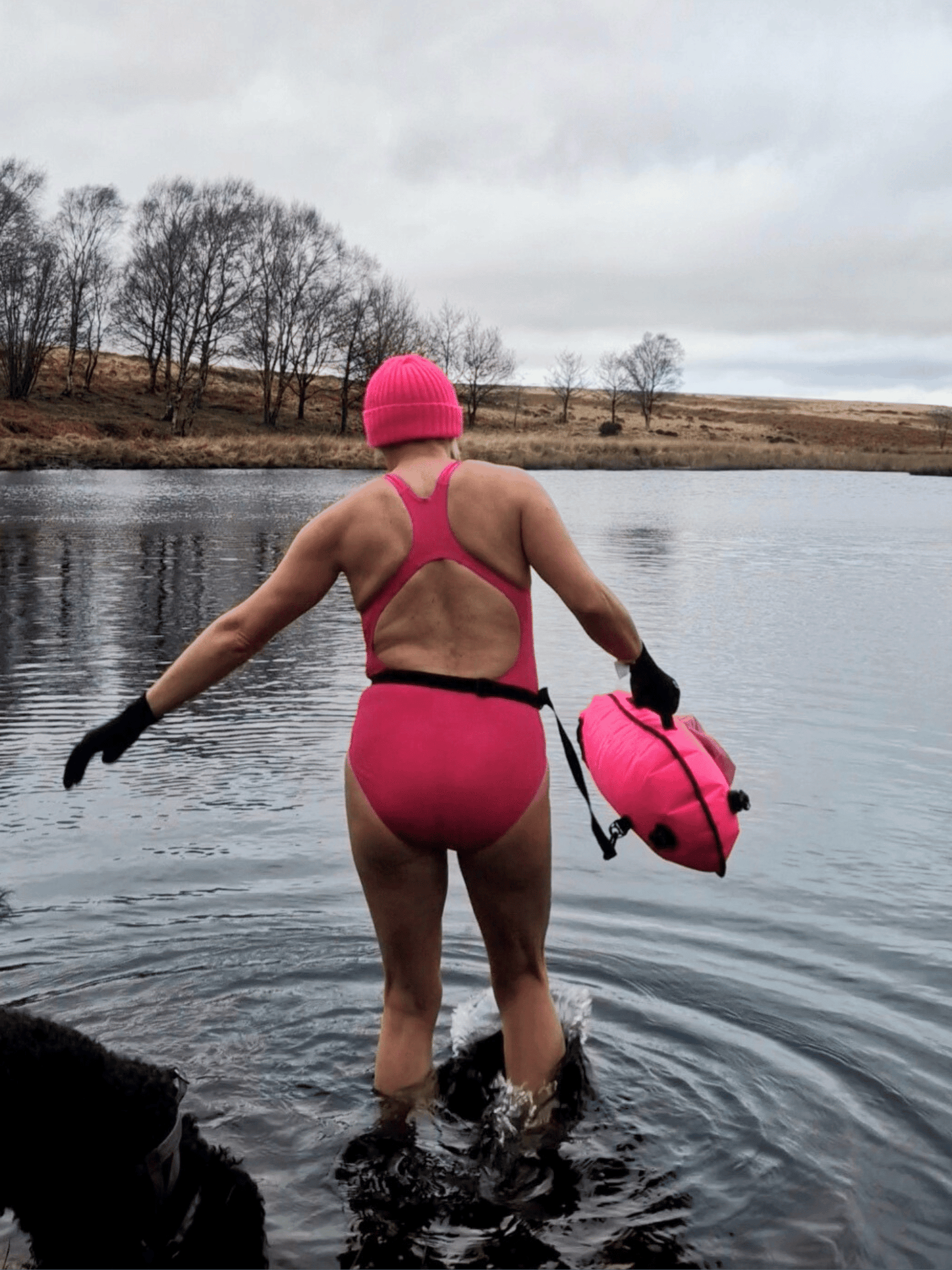 lady in pink hat, pink costume and carrying a pink tow float making her way into a lake