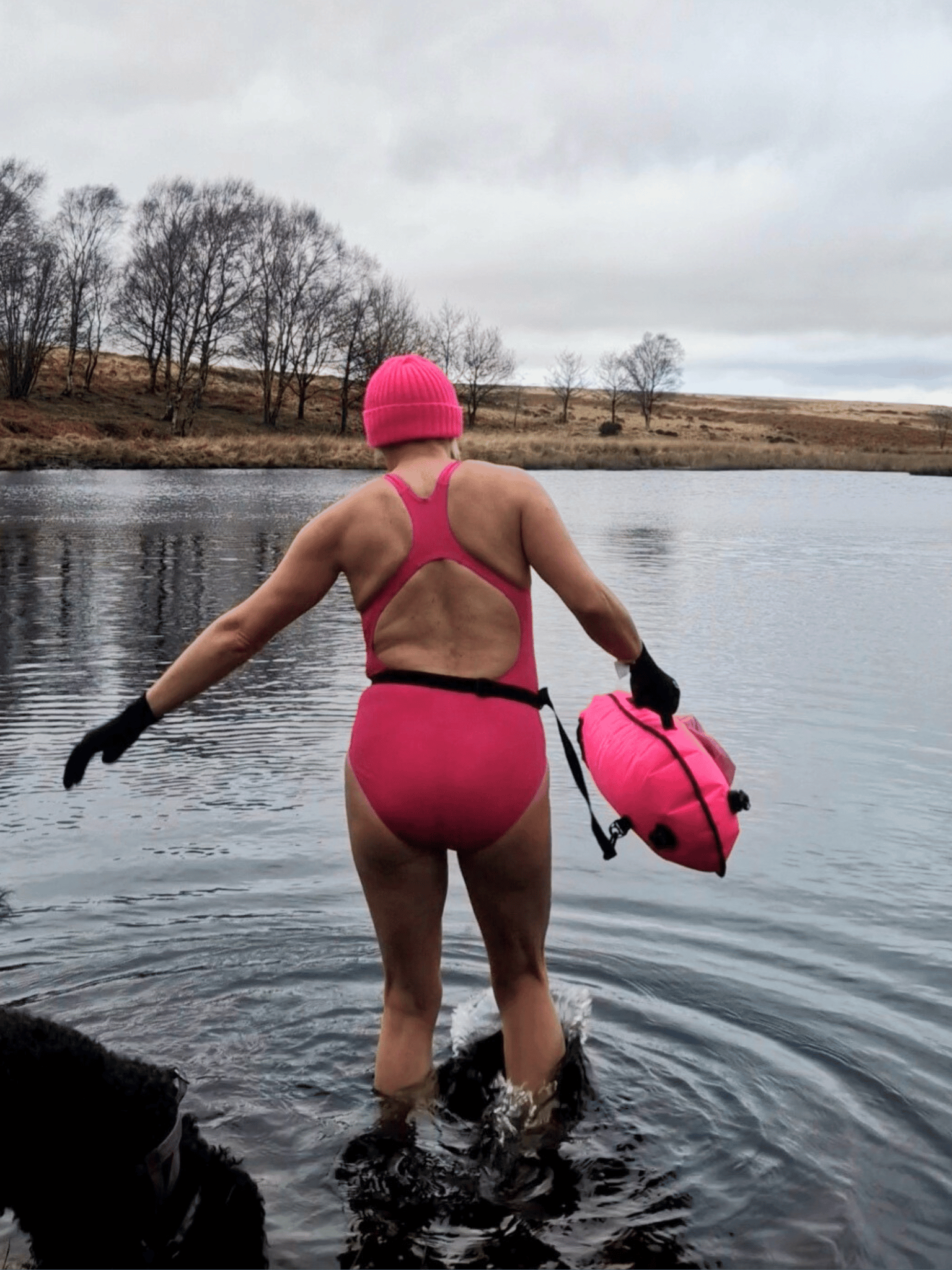 lady in pink hat, pink costume and carrying a  pink tow float making her way into a lake