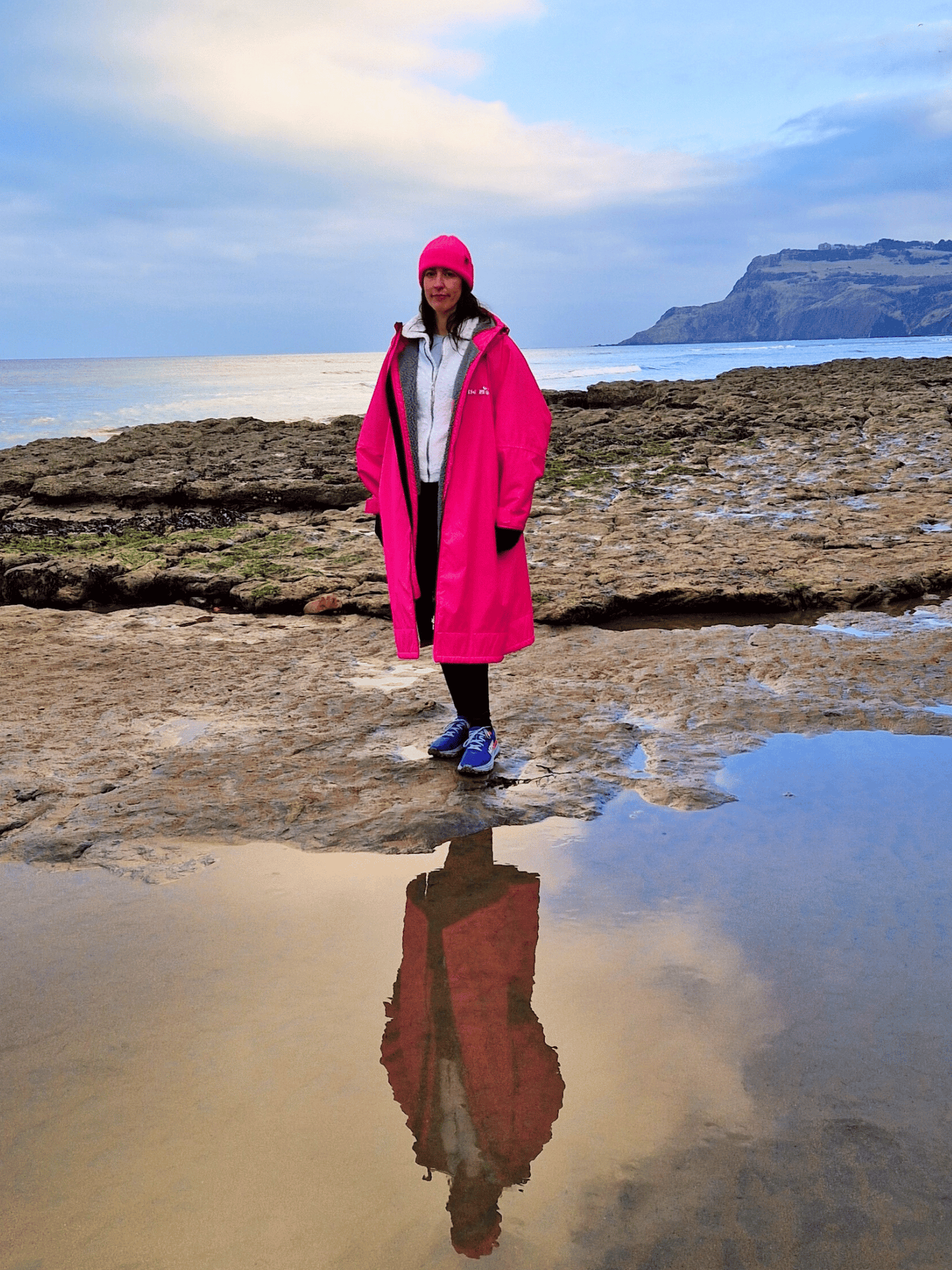 lady in a bight pink changing robe standing on a rocky coastline