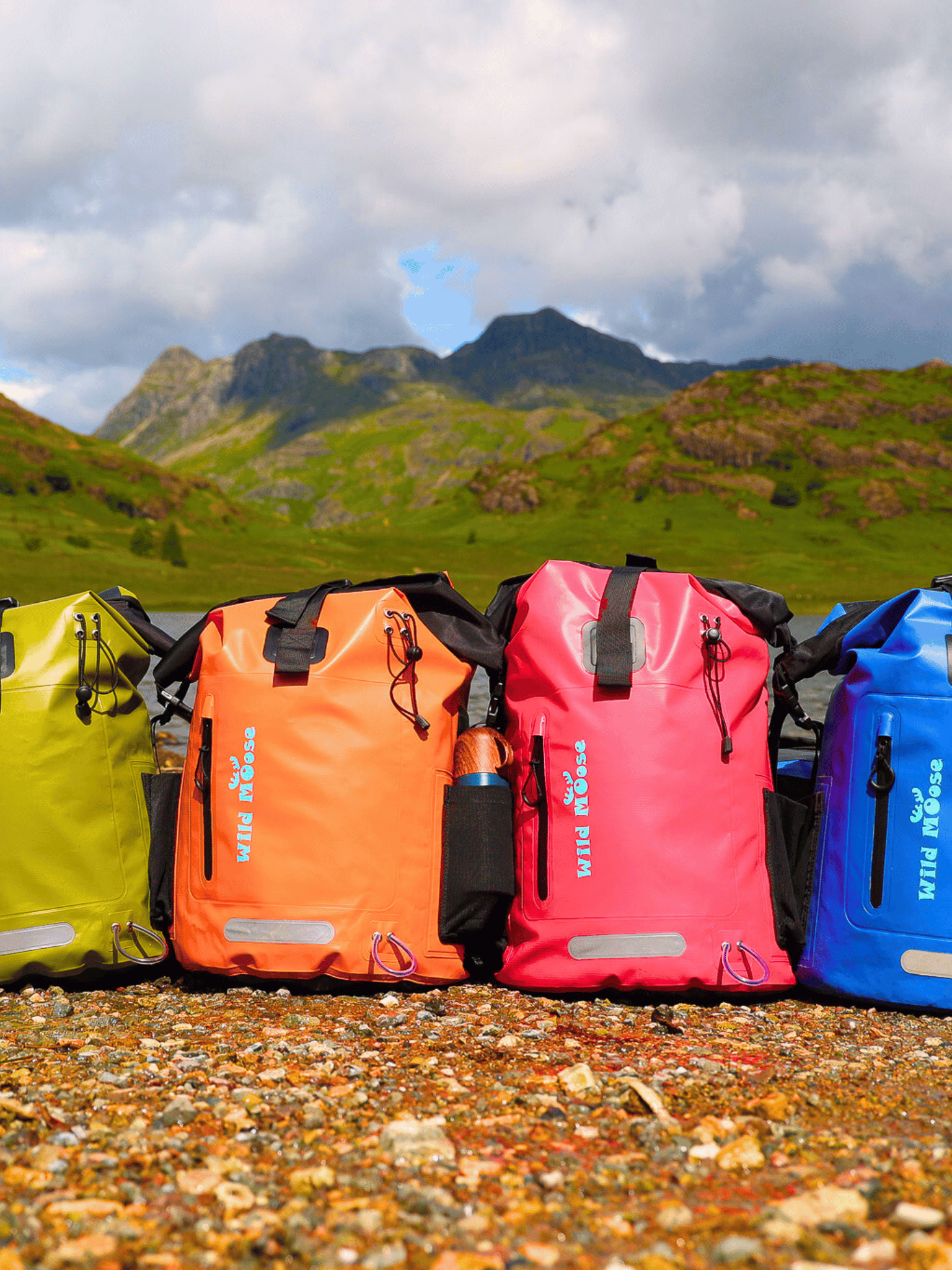 green, orange, pink and blue backpack on stony ground in the foreground with the Langdale Pikes in the background
