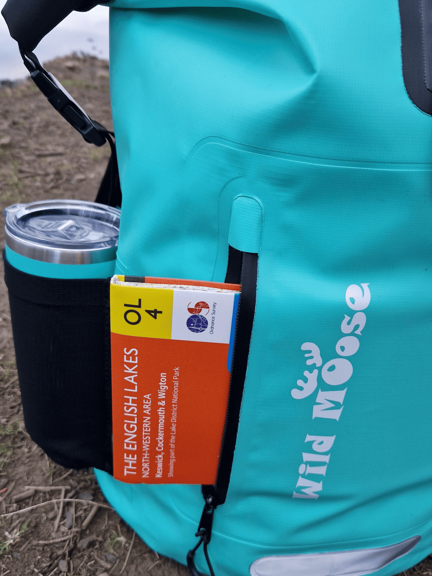 close up of the front pocket of a mint green coloured waterproof bag. There is an OS map sticking out. There is also a stretchy side pocket with a mint green flask in it