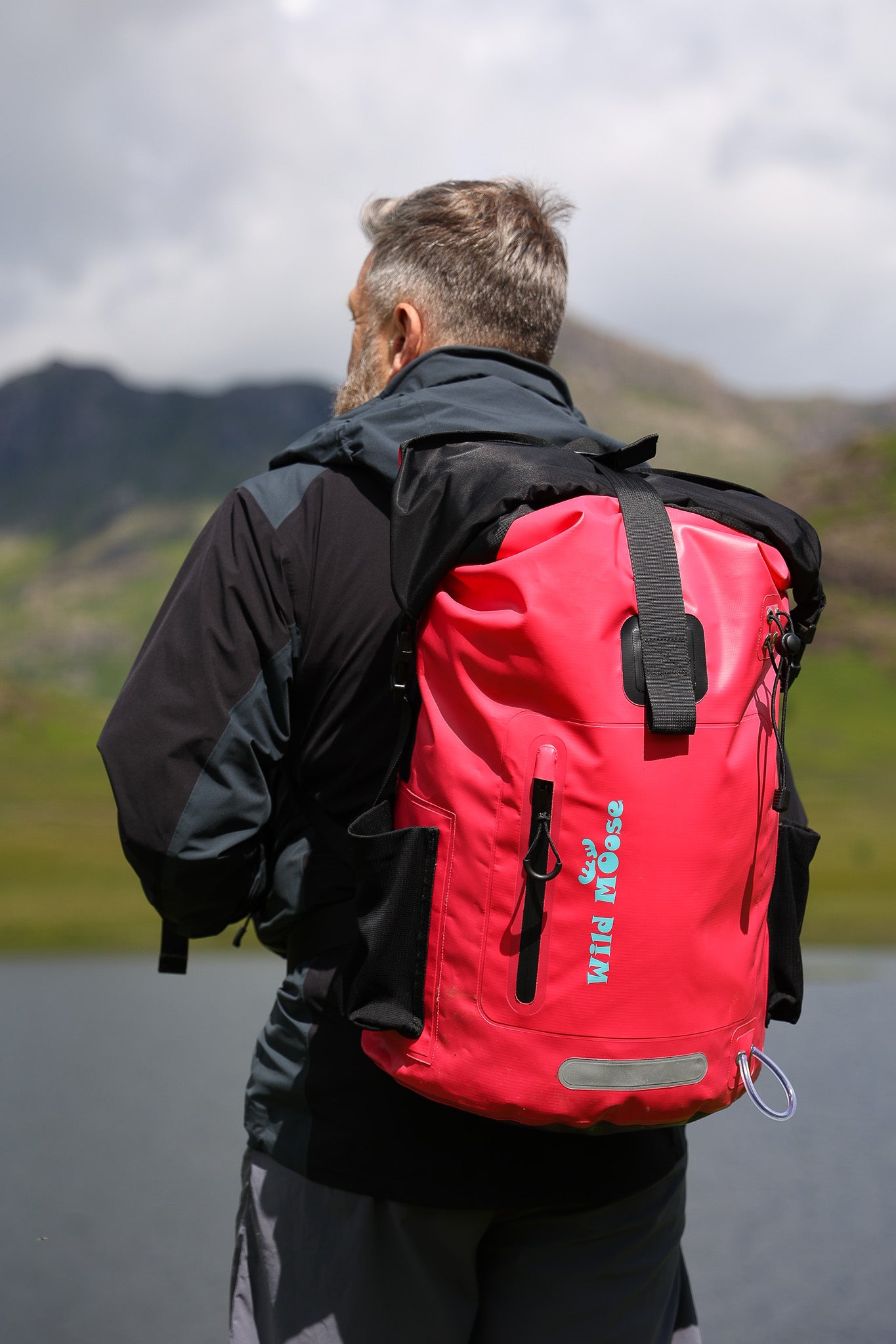 a man with his back to the camera wearing a bright pink backpack and looking out across a body of water