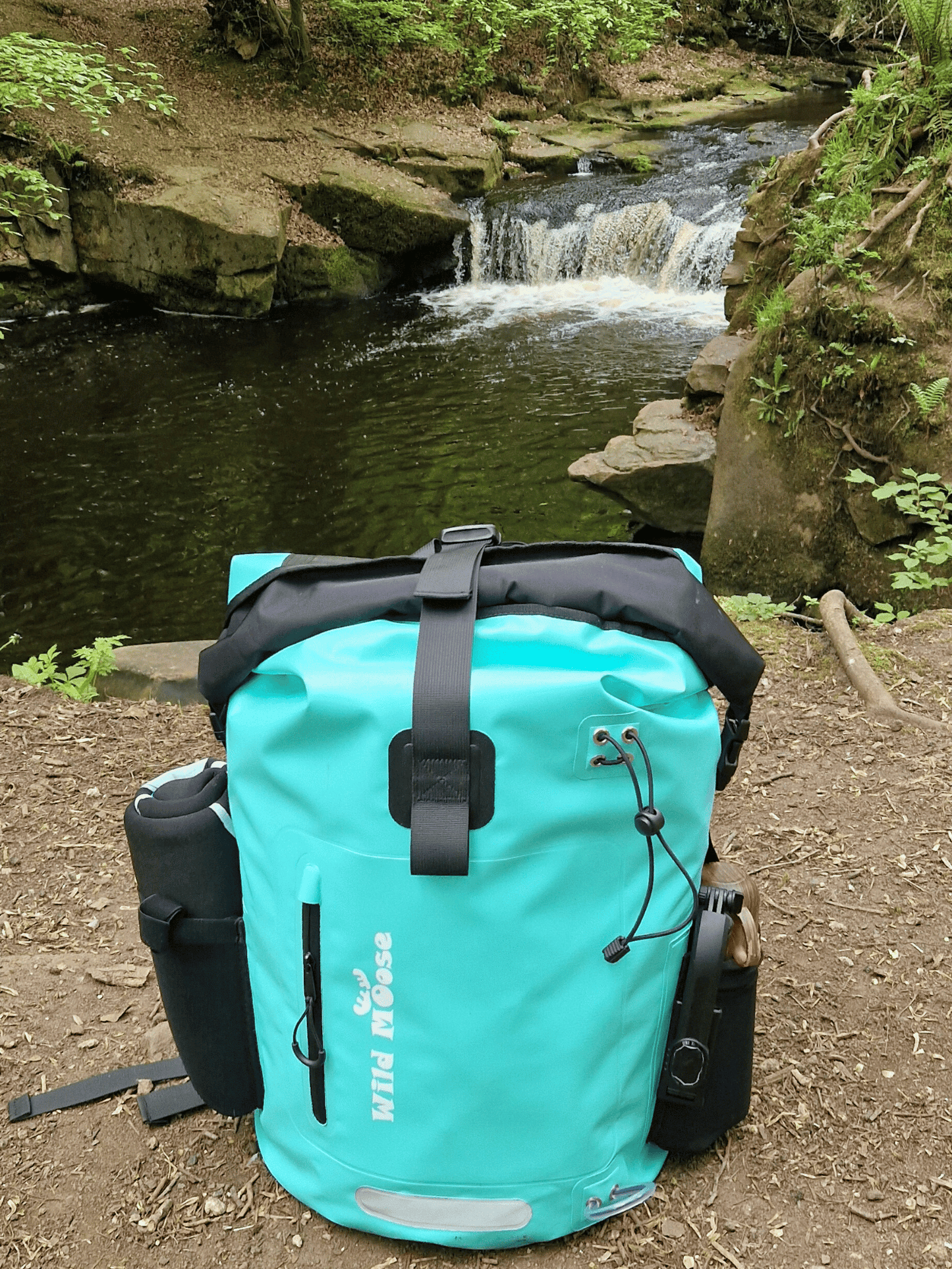 mint green coloured waterproof bag in the foreground with a small waterfall in the background
