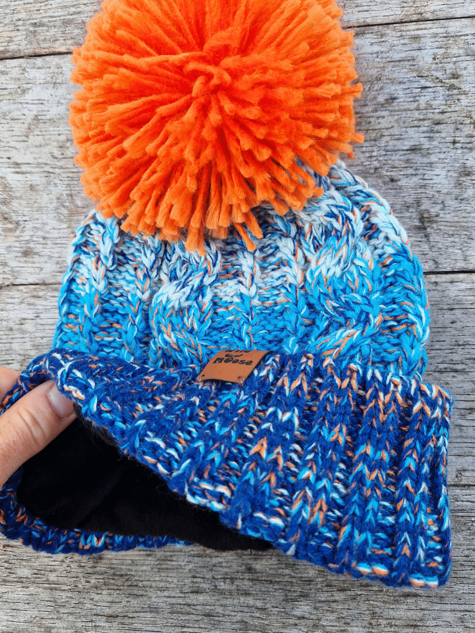 Blue knitted beanie with orange pom-pom on a wooden surface
