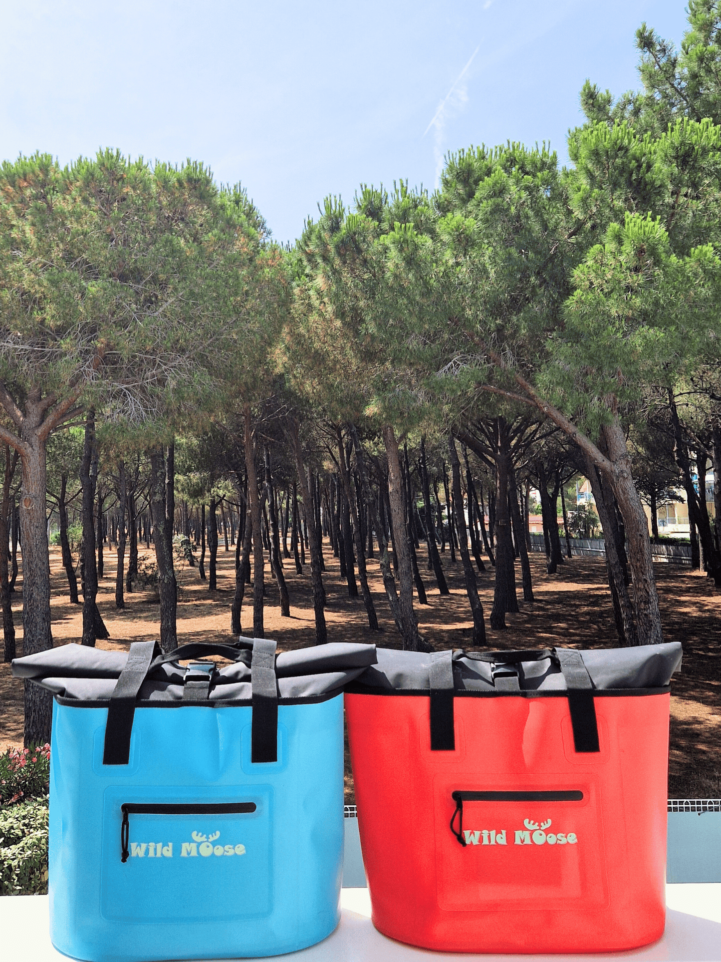 product shot a bright blue and a coral coloured tote bag with Wild Moose logo on a white wall in front of a pine forest