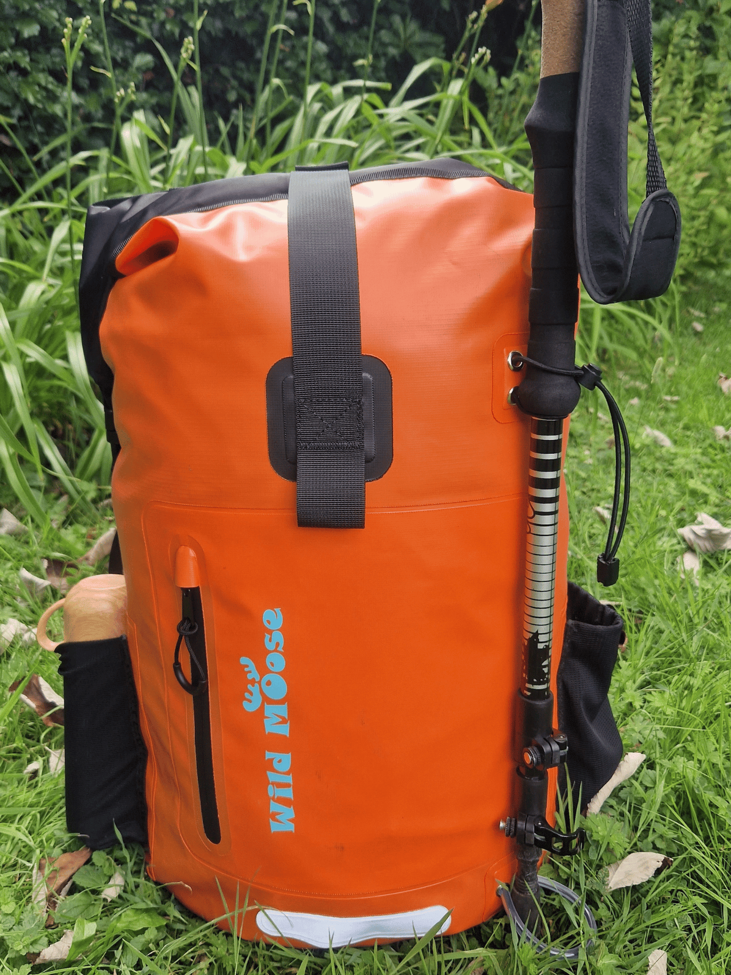 a flame orange backpack in the grass. a flask in the side pocket and a walking pole attached to the fornt