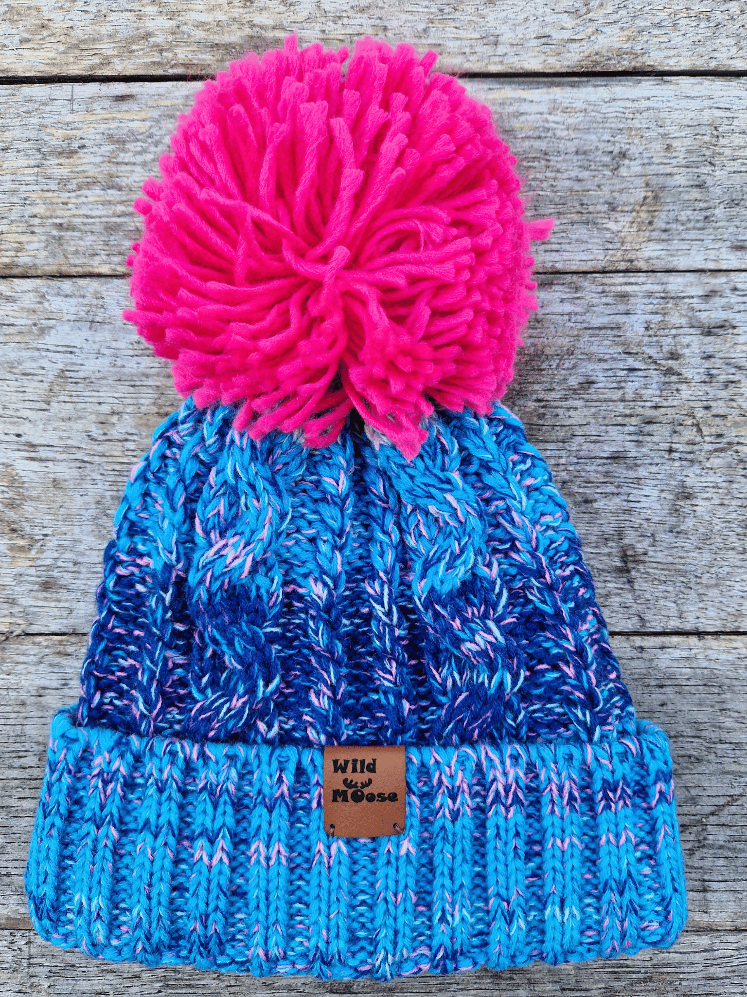Blue knitted beanie with a pink pom-pom on a wooden surface