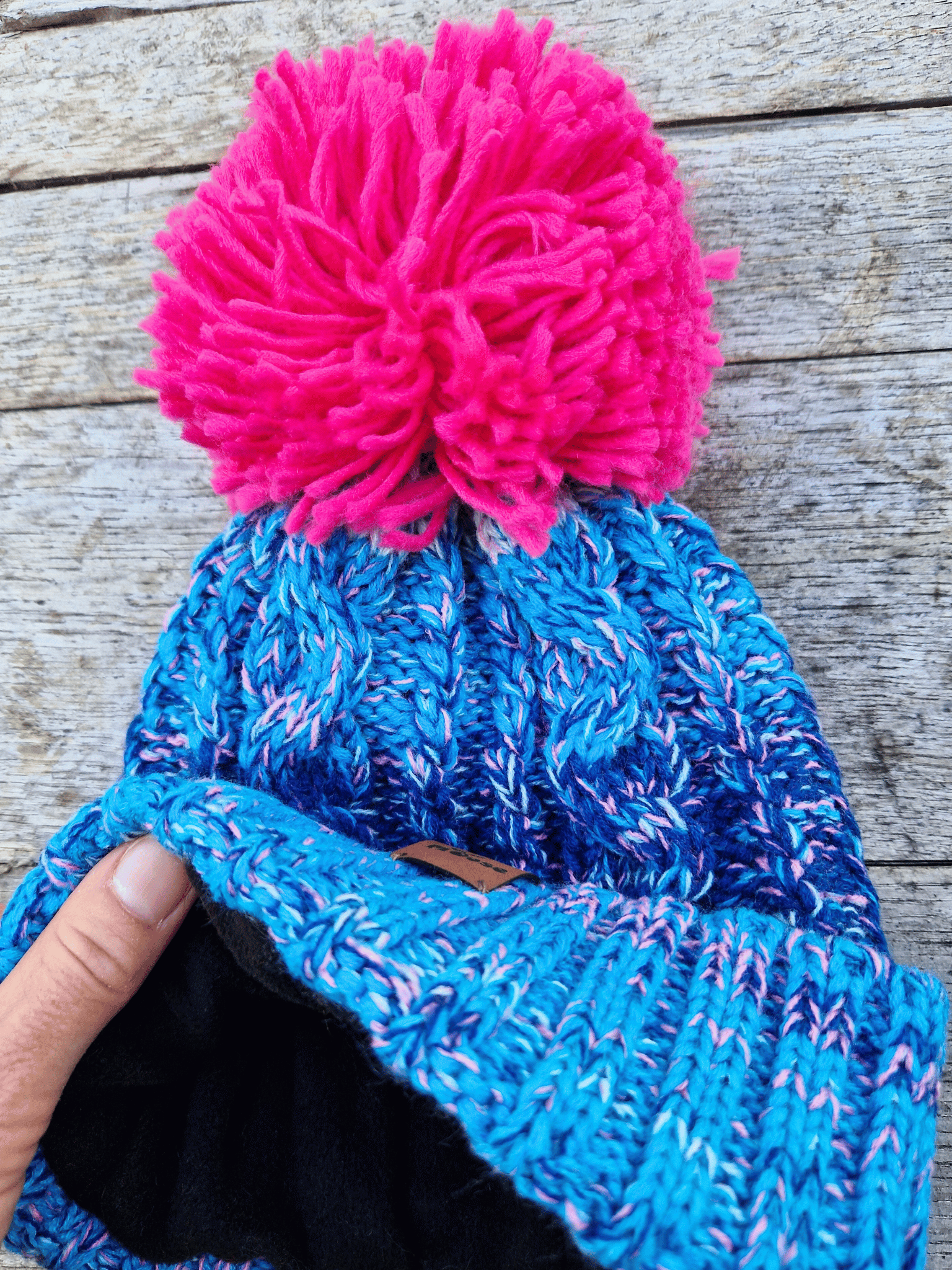 Blue knitted beanie with a pink pom-pom on a wooden surface