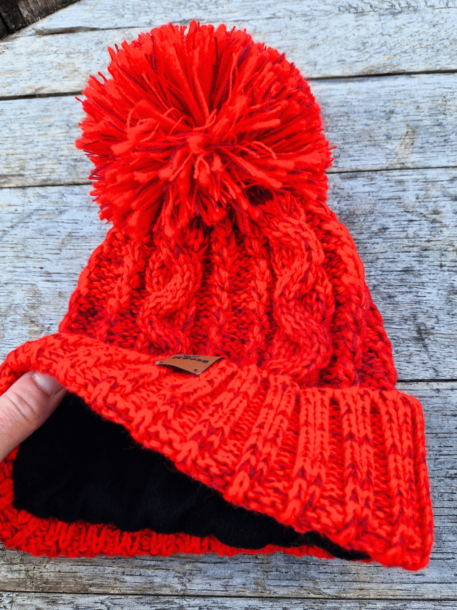 Red knitted beanie with pom-pom on a wooden surface