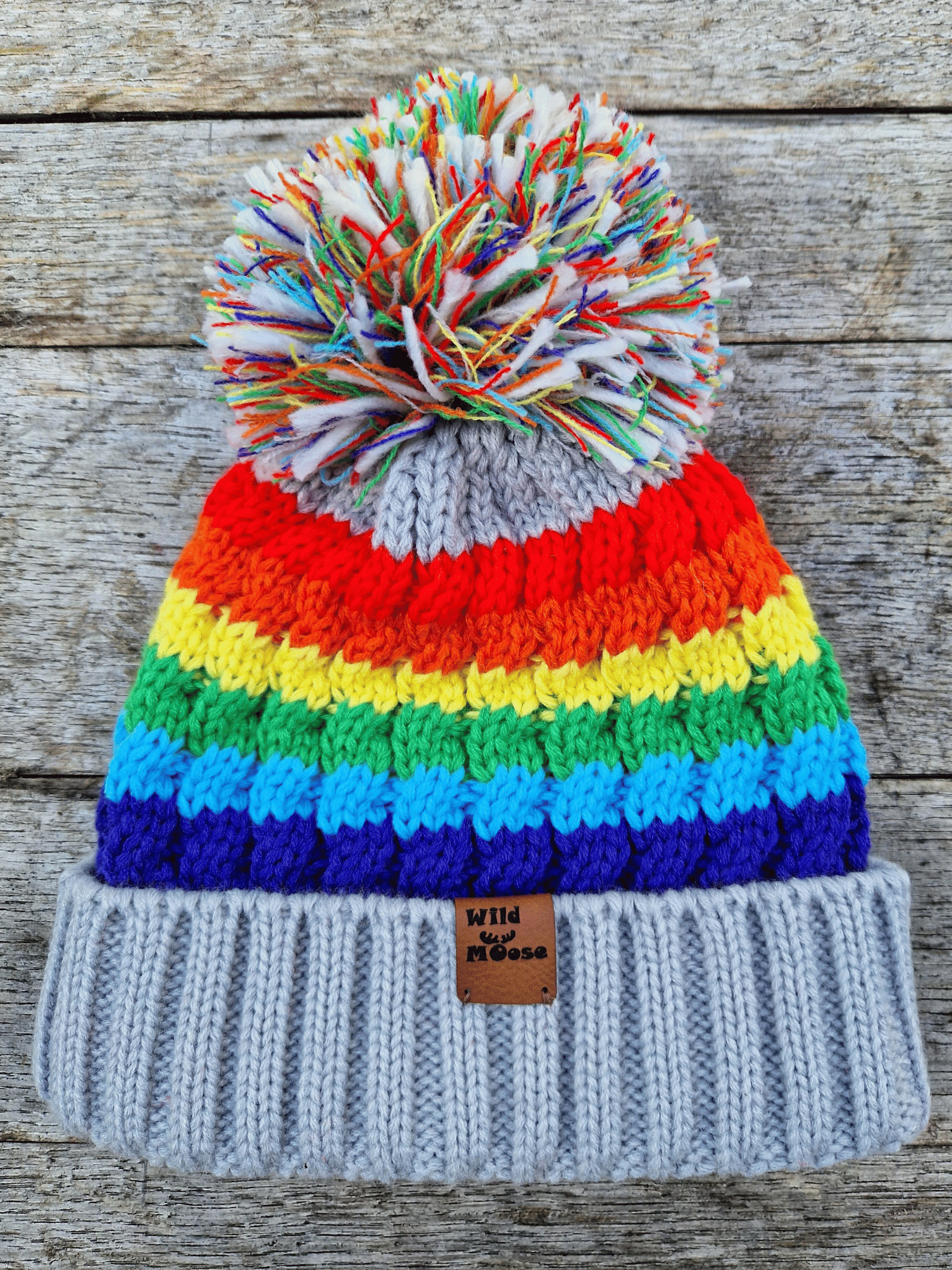 Colorful striped beanie with a pom-pom on a wooden surface