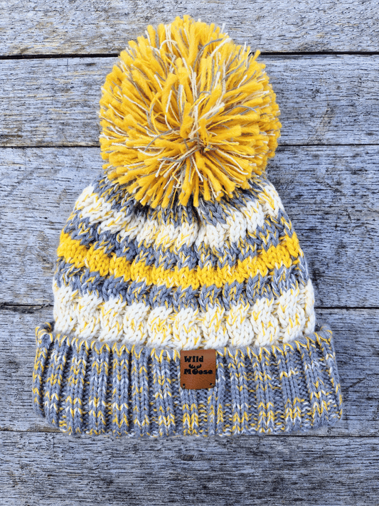 Knitted beanie with yellow and gray pattern on a wooden surface