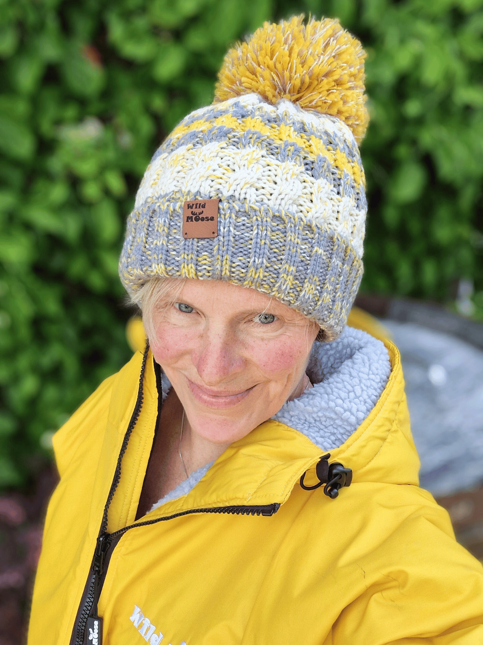 Person wearing a knitted beanie with a yellow pom-pom and a yellow jacket outdoors.
