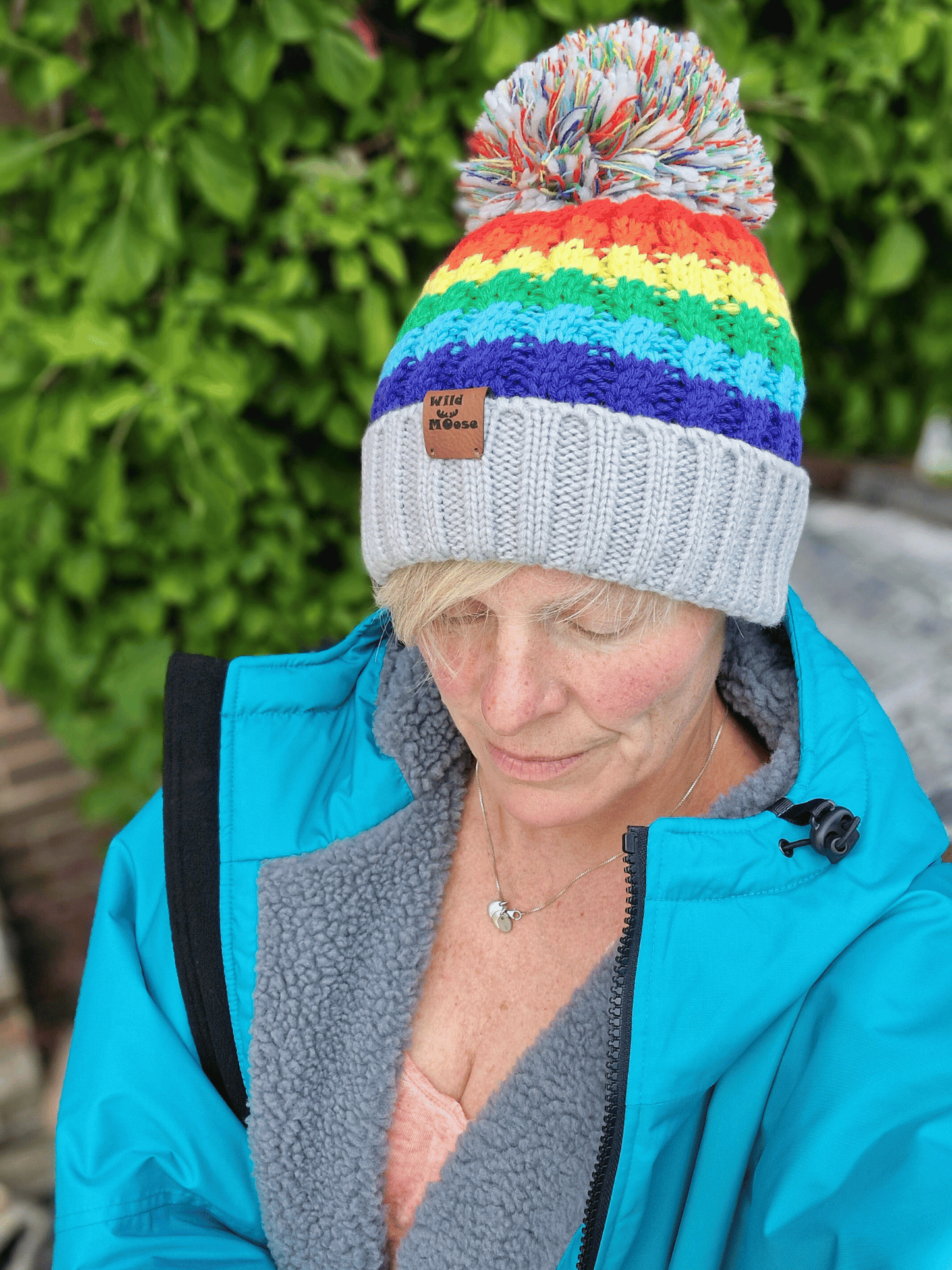 Person wearing a colourful striped beanie and teal changing robe with a blurred green background