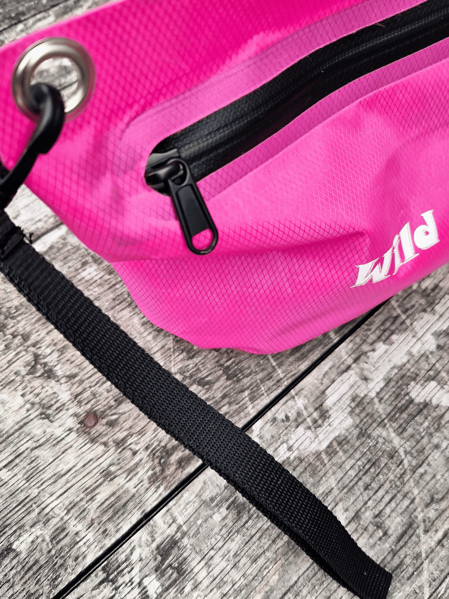 Pink zip bag with black wrist strap and 'Wild Moose' branding on a wooden surface