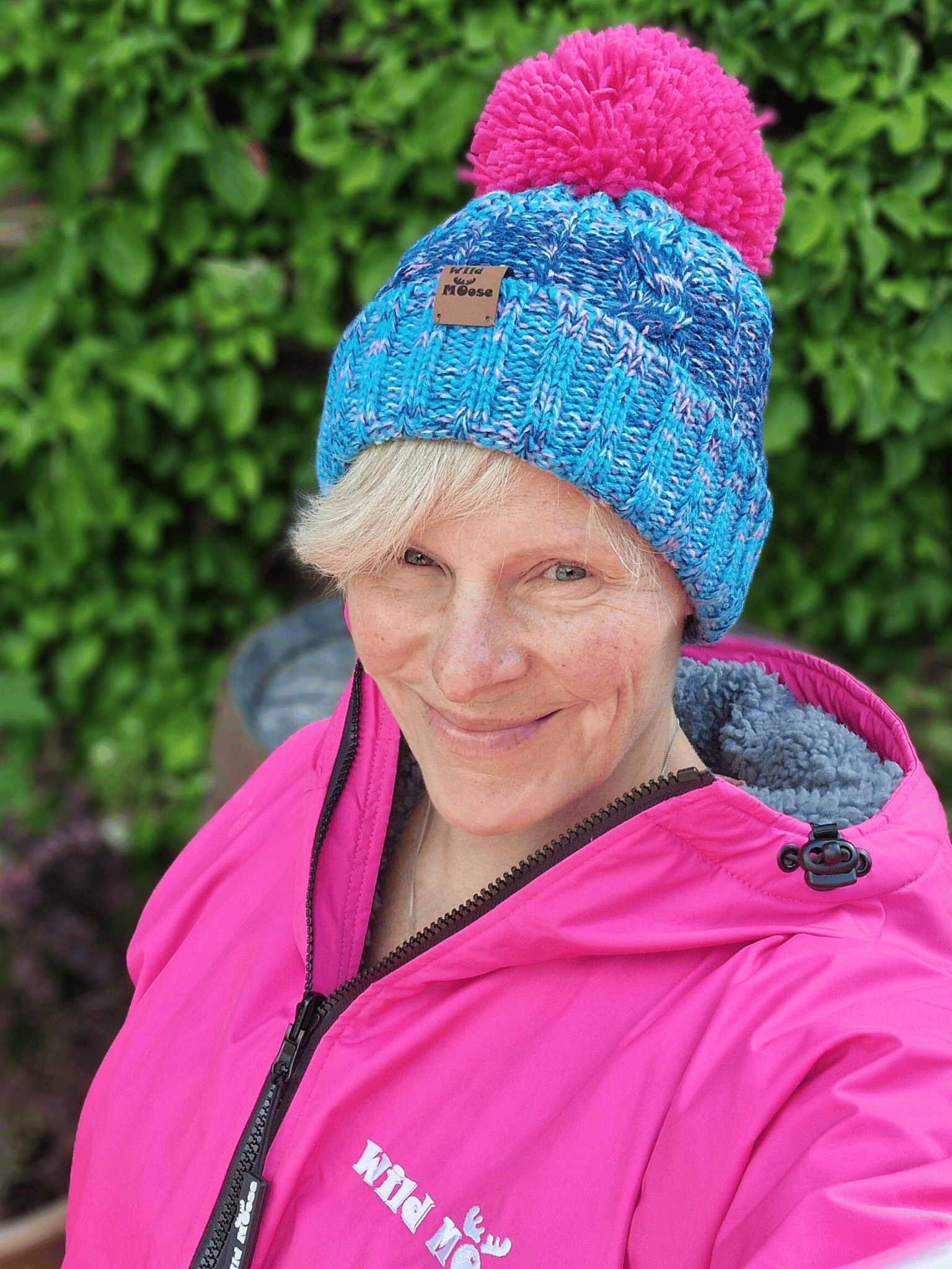 Person wearing a blue knit hat with a pink pom-pom and a pink changing robe with visible branding.