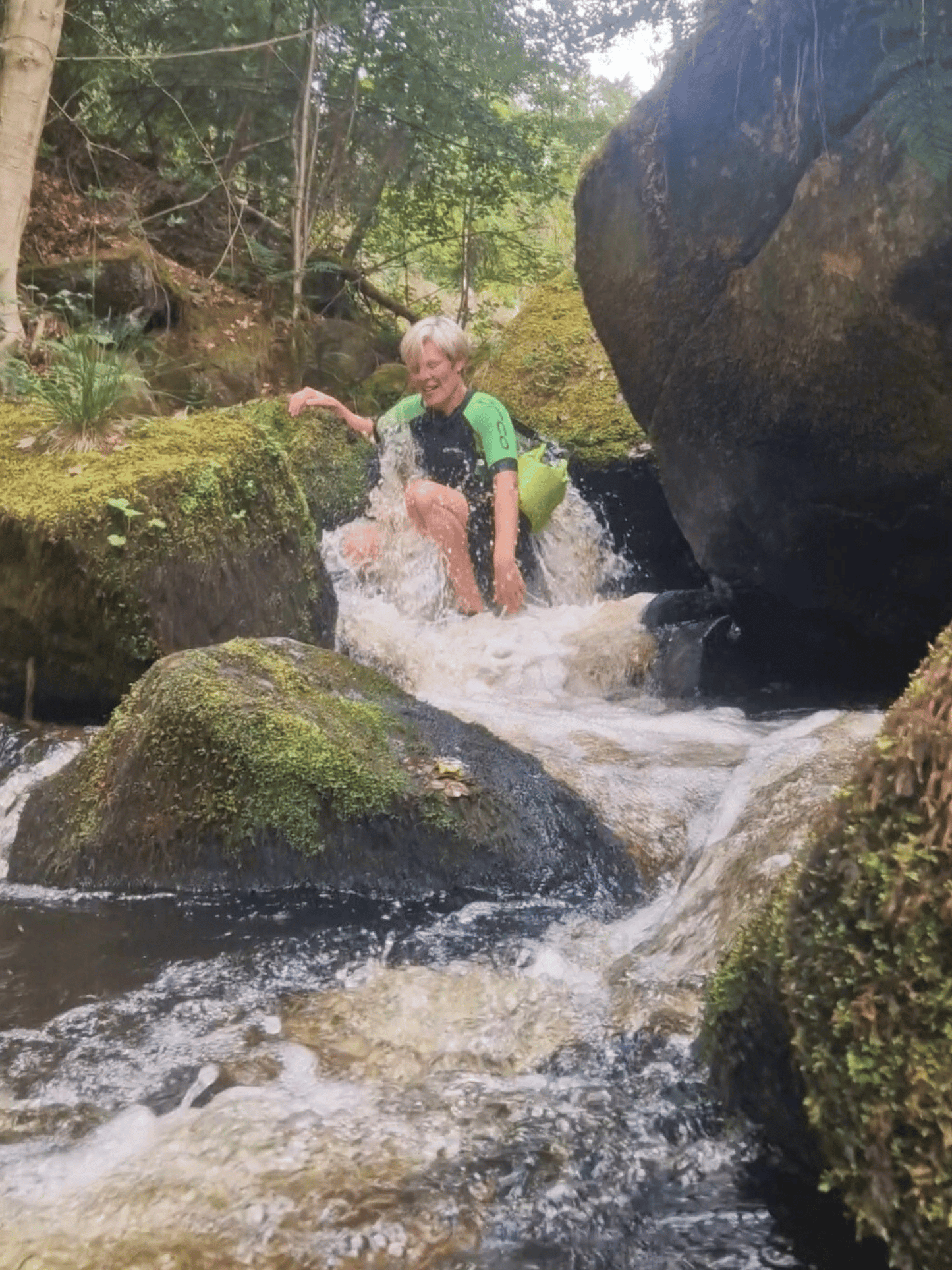 lady in wetsuit in small waterfall with 5L green dry bag over shoulder