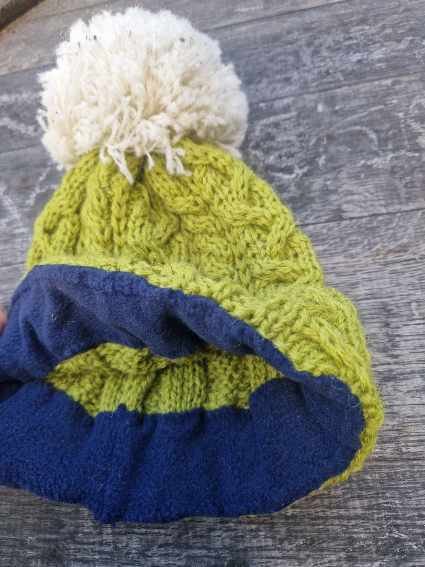 showing the black lining of a pea green bobble hat with cream pom pom