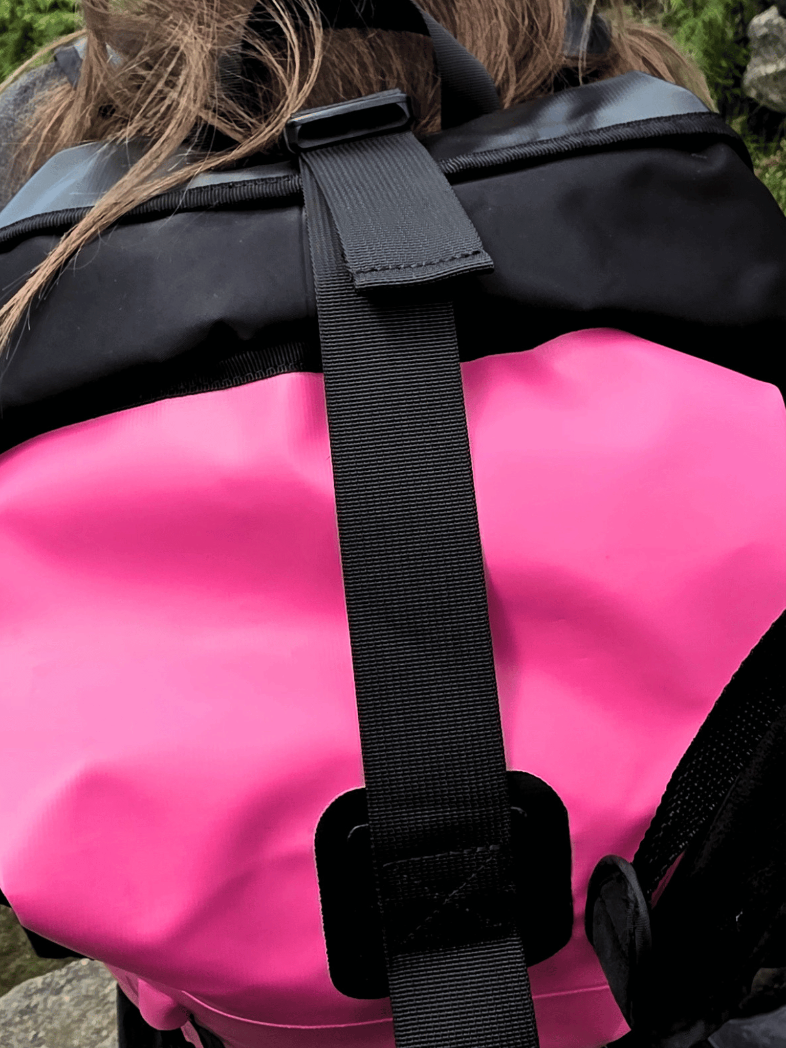 Close-up of a waterproof backpack with a bright pink lower section and black upper section, featuring a black strap and buckle closure.
