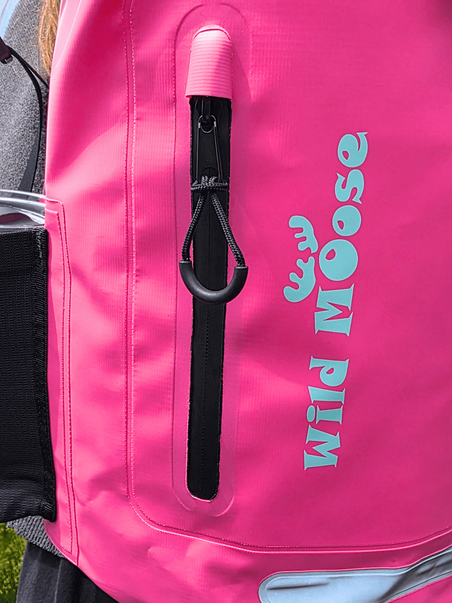 Close-up of a bright pink backpack with a vertical black zipper pocket, and turquoise 'WILD MOOSE' logo printed on the side.