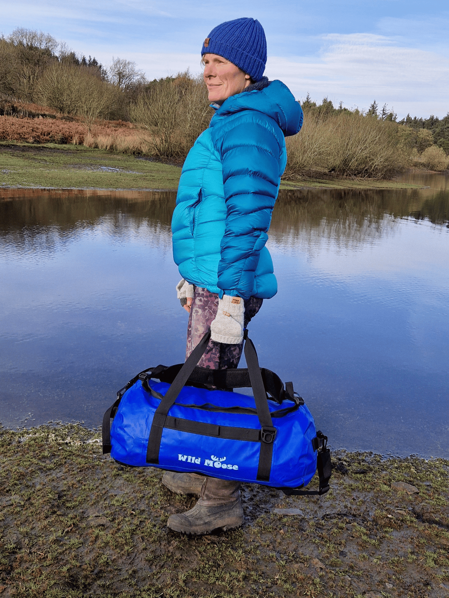 lady stood by water carrying an electric blue duffel bag by the grab handles