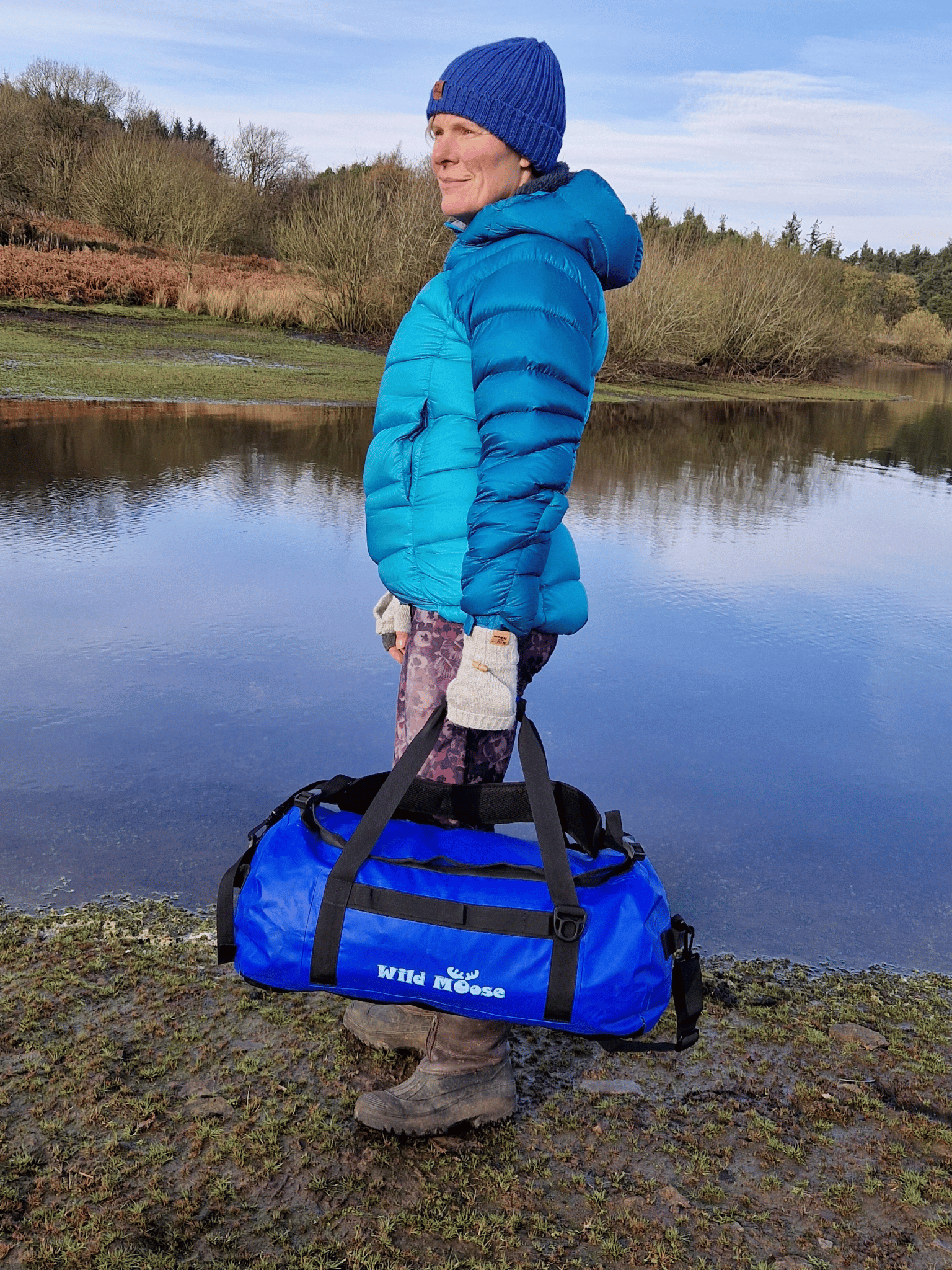 lady stood by water carrying an electric blue duffel bag by the grab handles