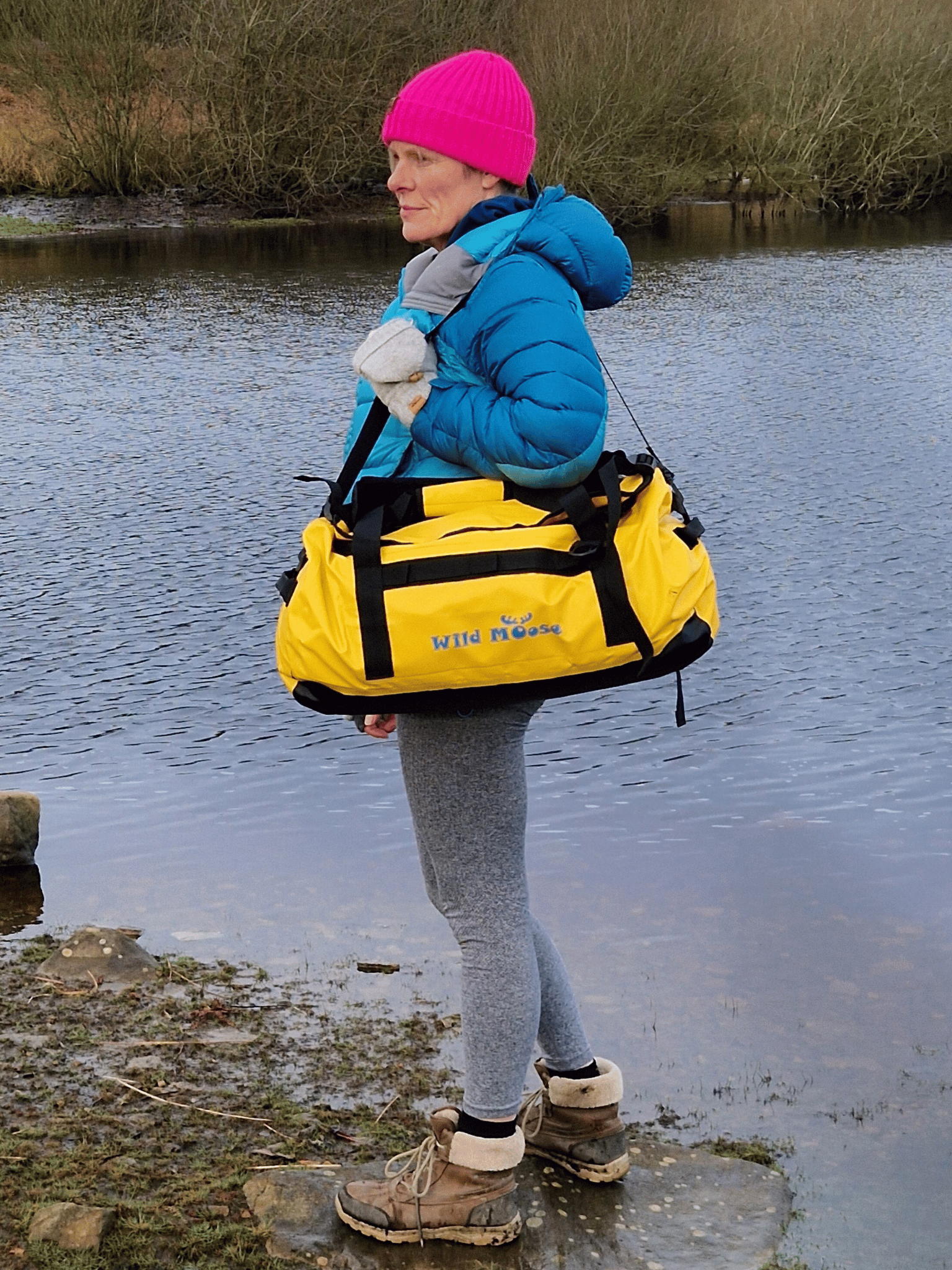 lady stood by water carrying a bright yellow duffel bag over her shoulder