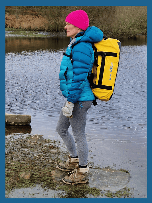 lady stood by water carrying a bright yellow duffel bag on her shoulders