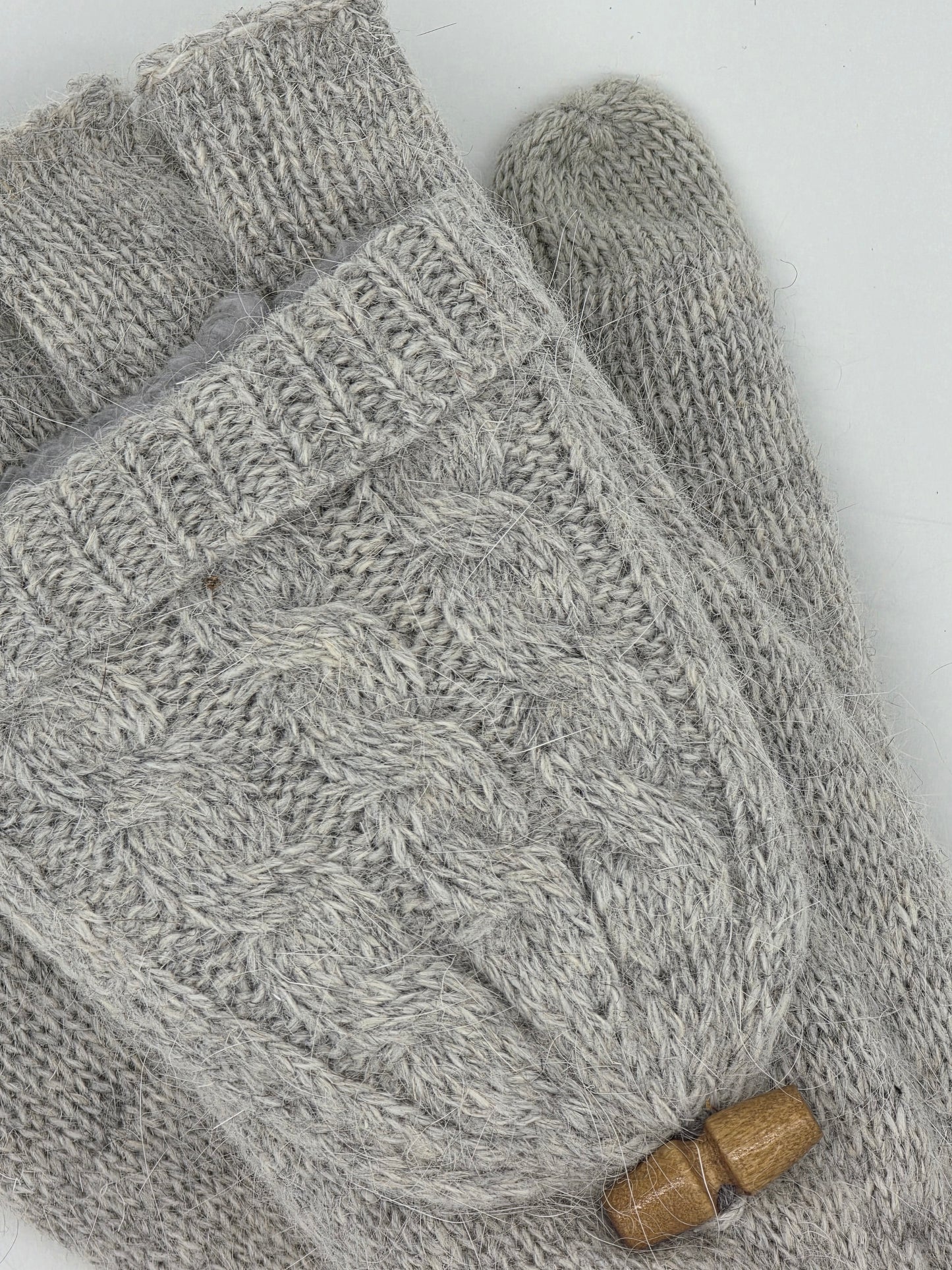 close up of a grey knit fingerless mittens on a white background.