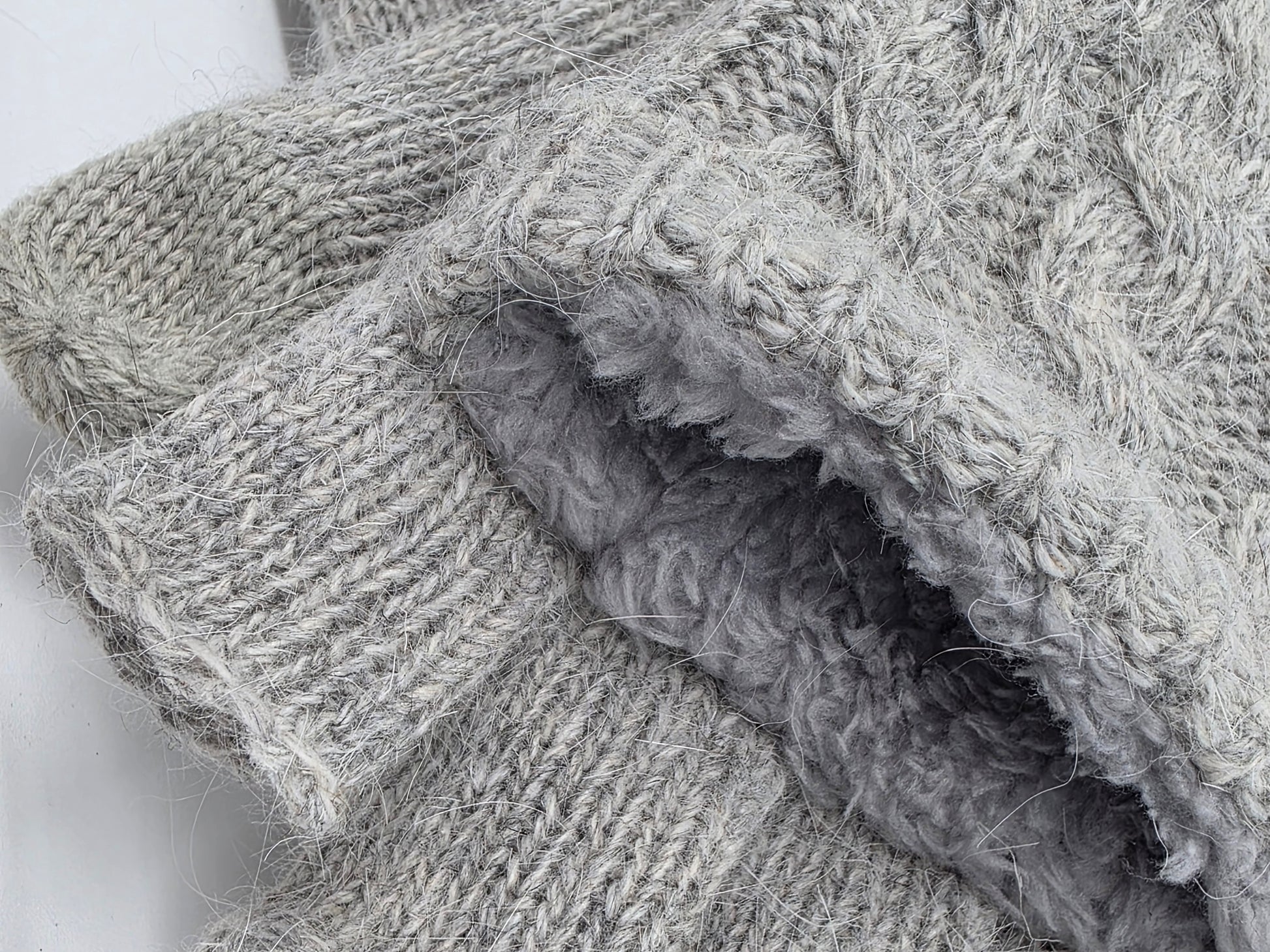 close up of the knit and fluffy inside of  2 grey mittens on a white backdrop.