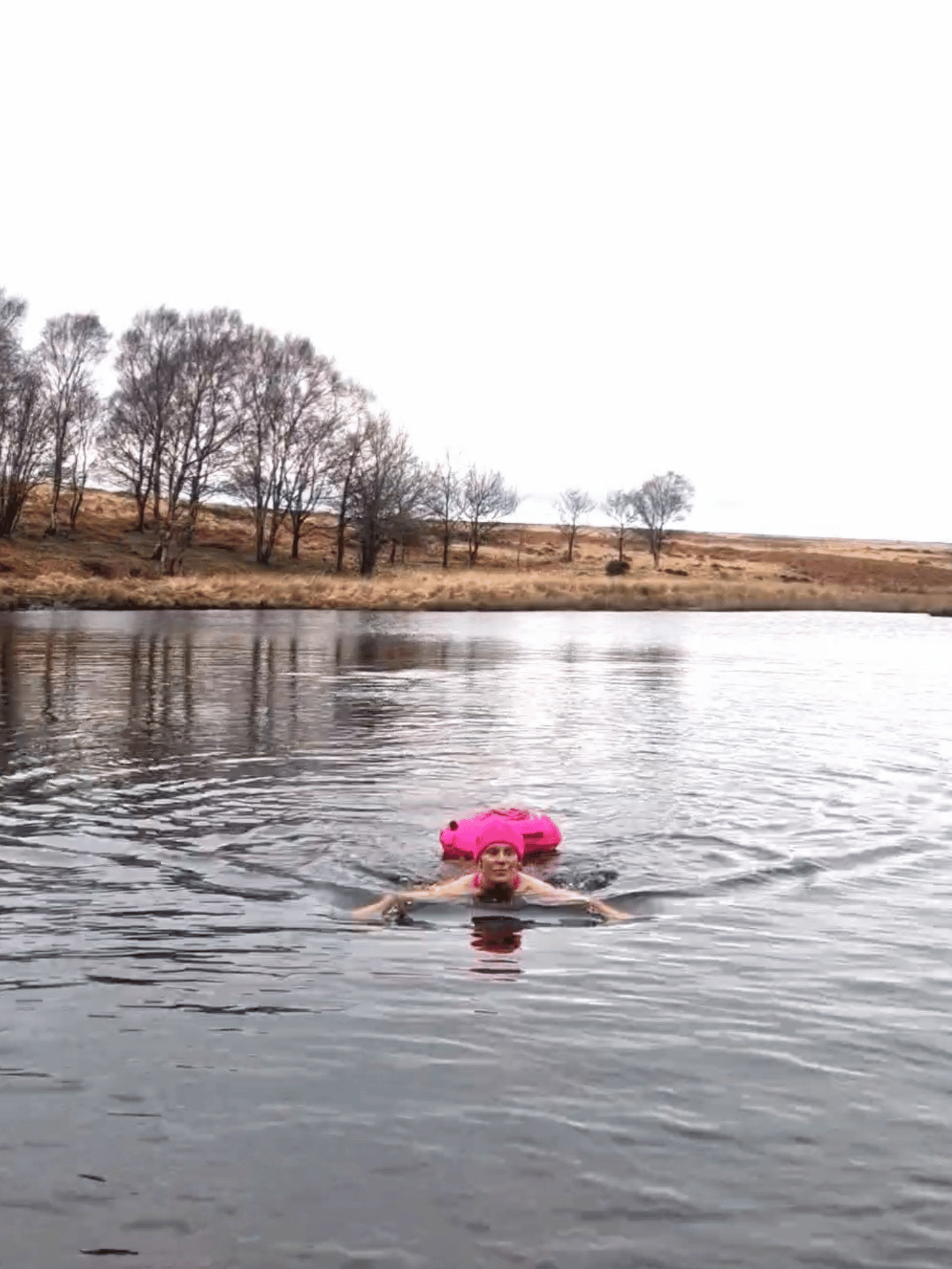 lady swimming in a lake with a pink tow float and a pink beanie hat