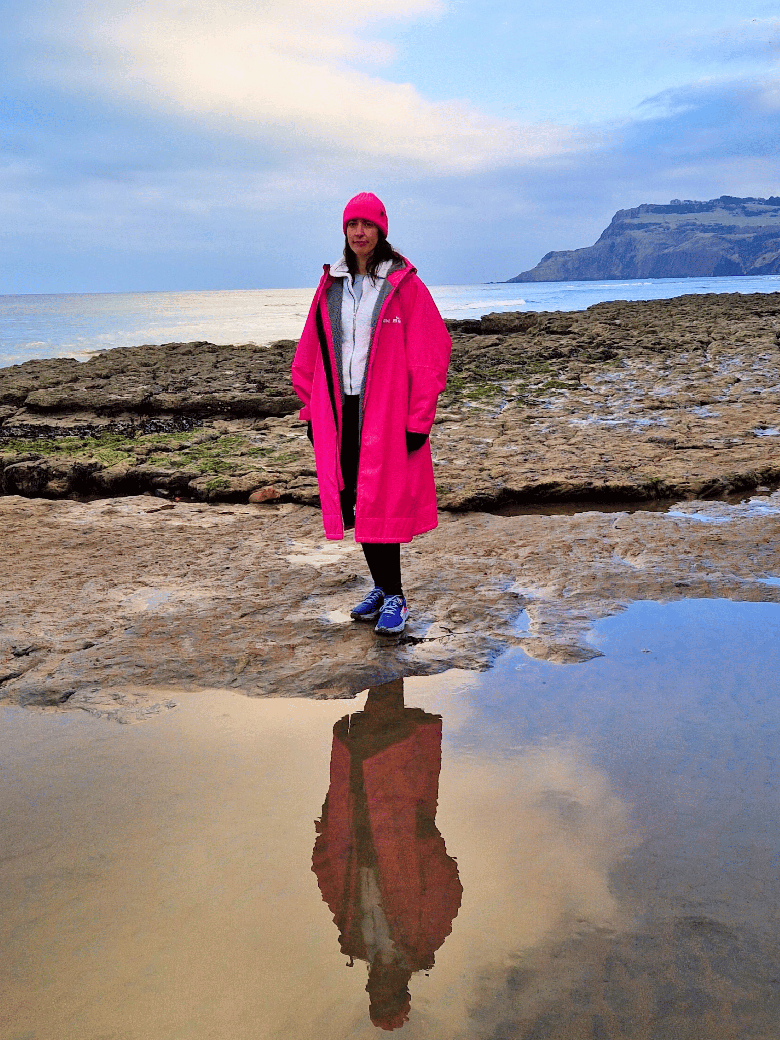 lady in a bight pink changing robe standing on a rocky coastline