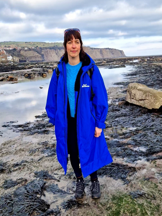 lady in an electric blue changing robe standing on a rocky shoreline