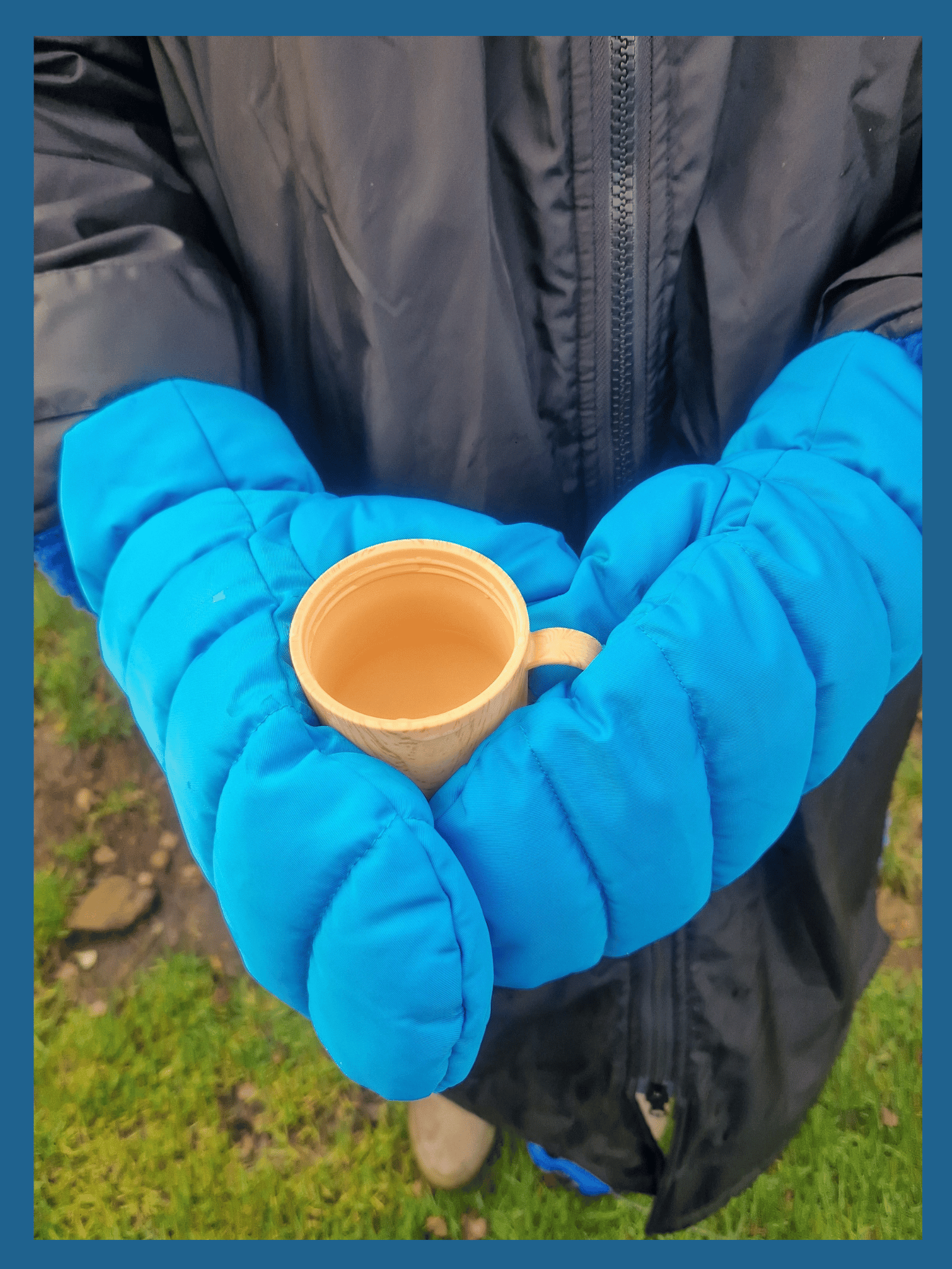 a close up shot of a pair of sky blue coloured, waterproof mittens. The mittens are cradling a cup.