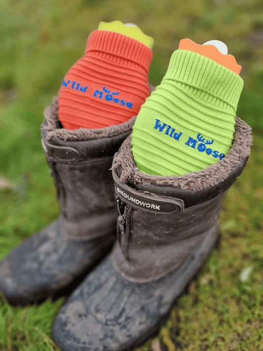 brightly coloured mini hot water bottles in a knitted cover in orange and lime green - placed in a pair of muddy boots