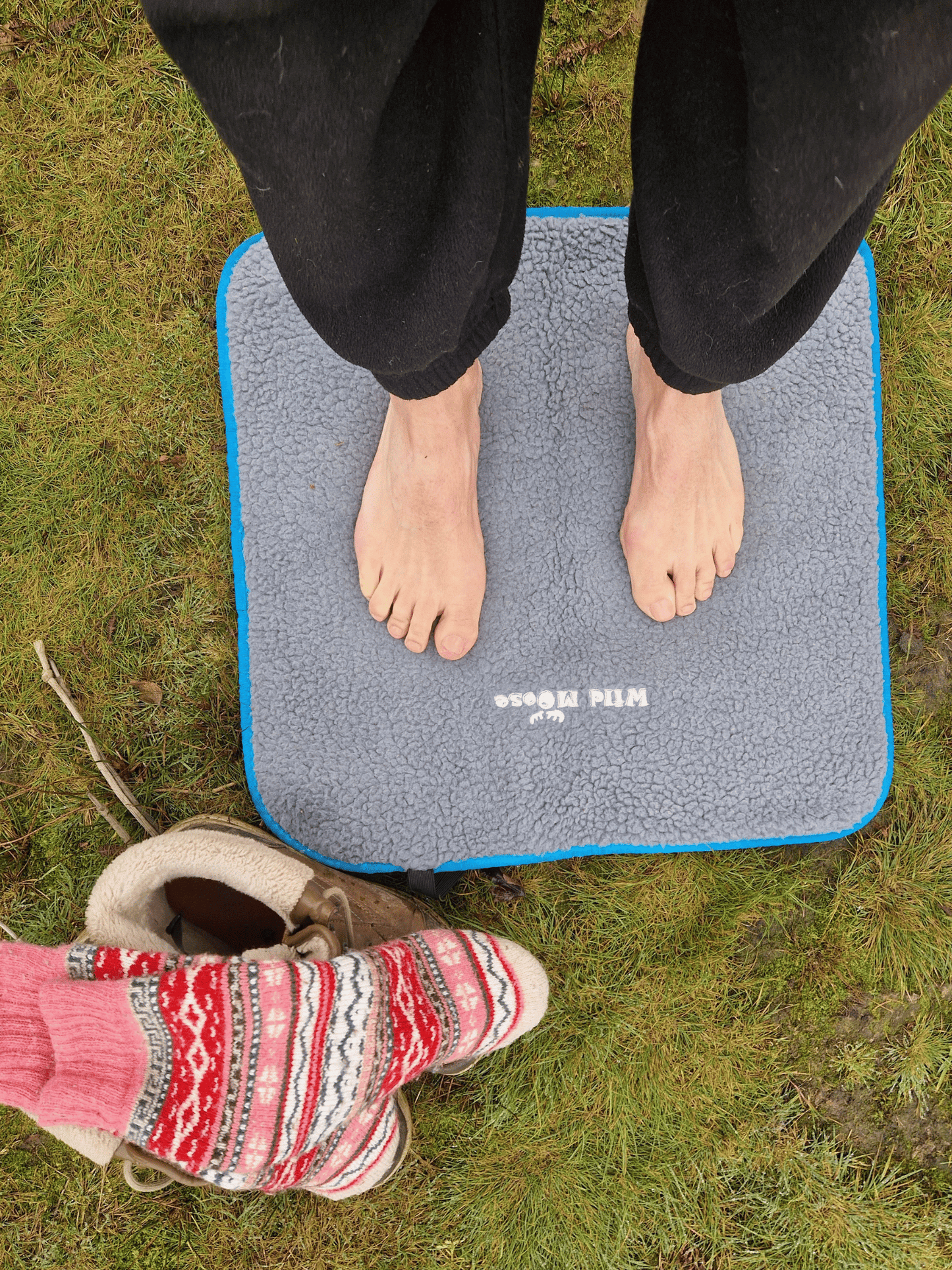 bare feet on a fleece lined changing mat on grass, with a pair of boots and thick colourful, nordic/scandi style socks next to the mat