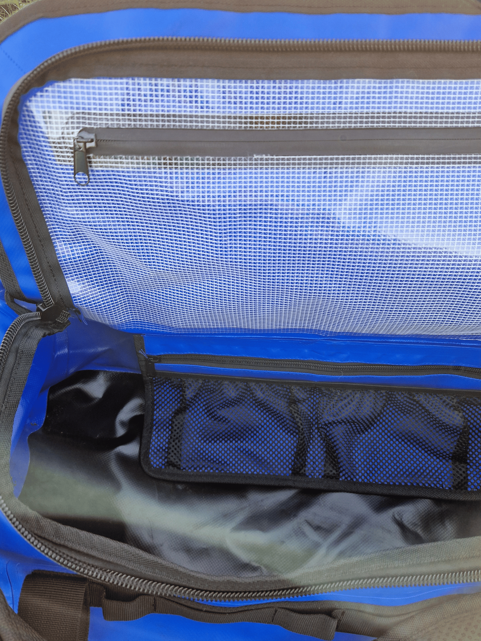 inside of the electric blue duffel bag. There is a waterproof, zipped pocket on the closing lid of the bag and mesh pockets to the back wall