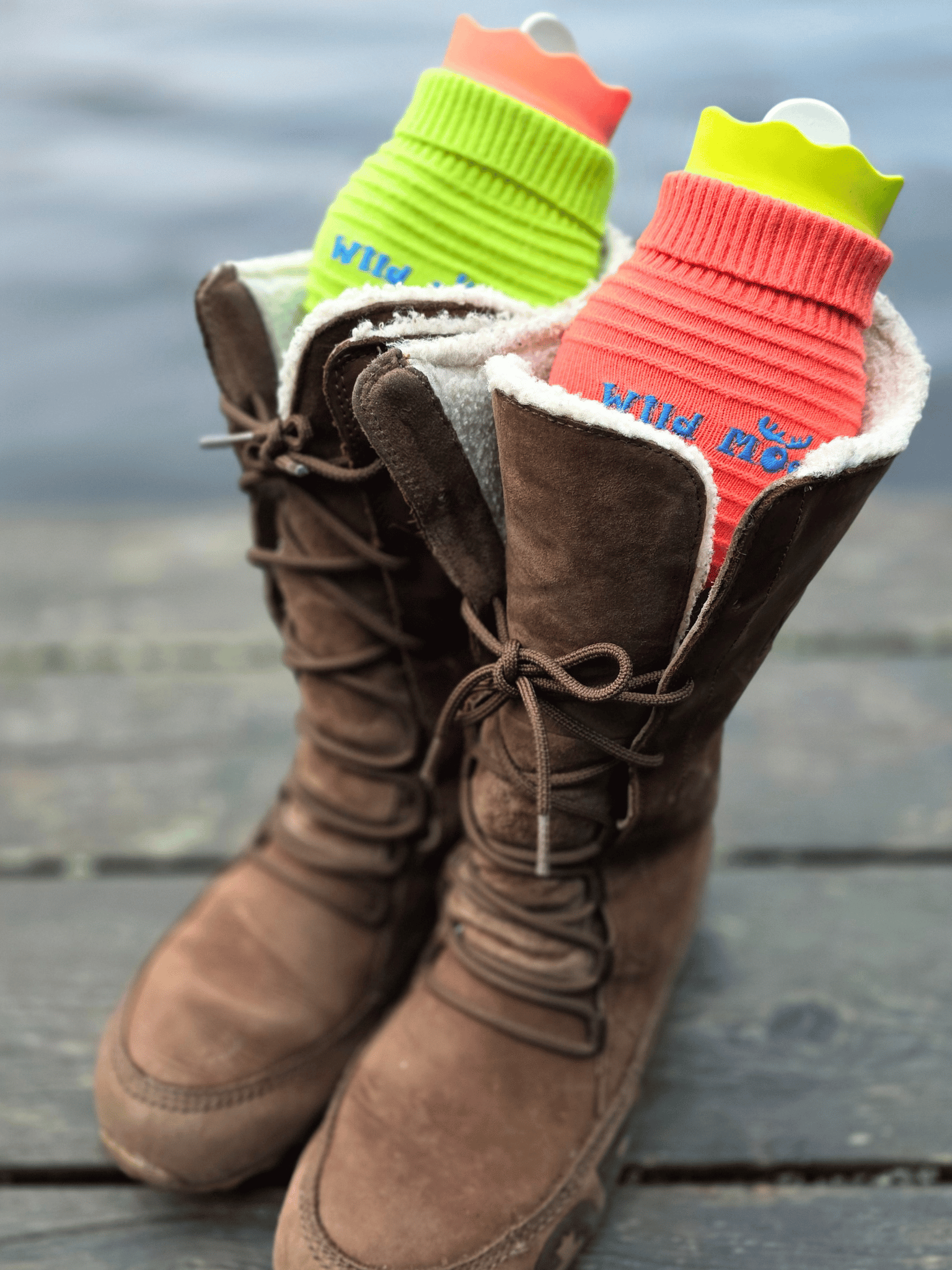 mini hot water bottles in a knitted cover in a pair of fleece lined boots. One is green and the other orange