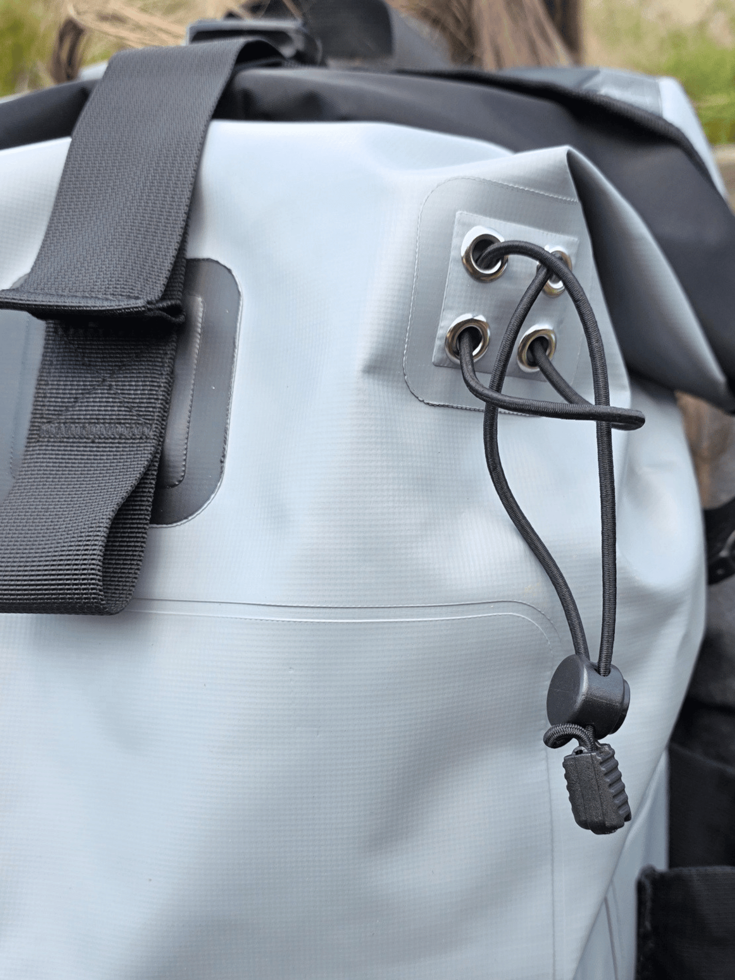 Close-up of a light gray waterproof backpack with black straps and walking pole loops.