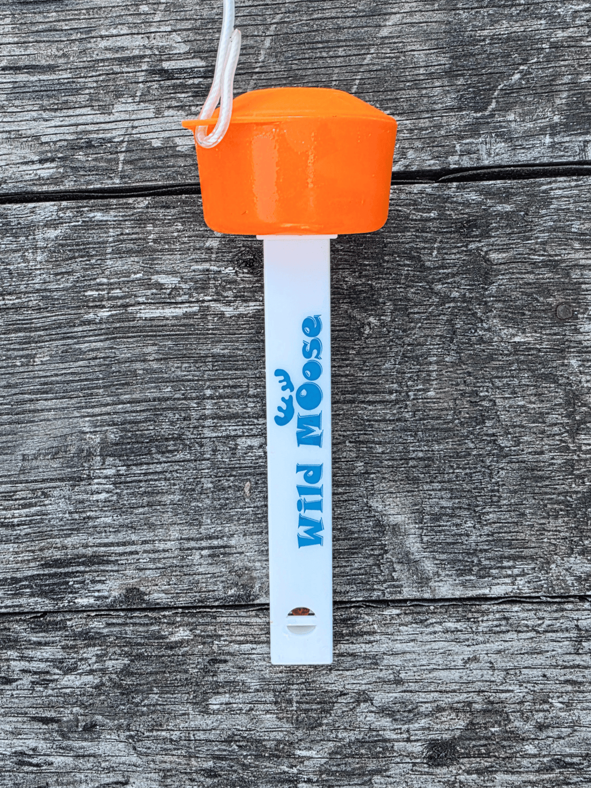 The back of a floating thermometer for outdoor swimming. It has an orange cap and white body printed with the brand name 'Wild Moose' in blue, shown against a weathered grey wood background.