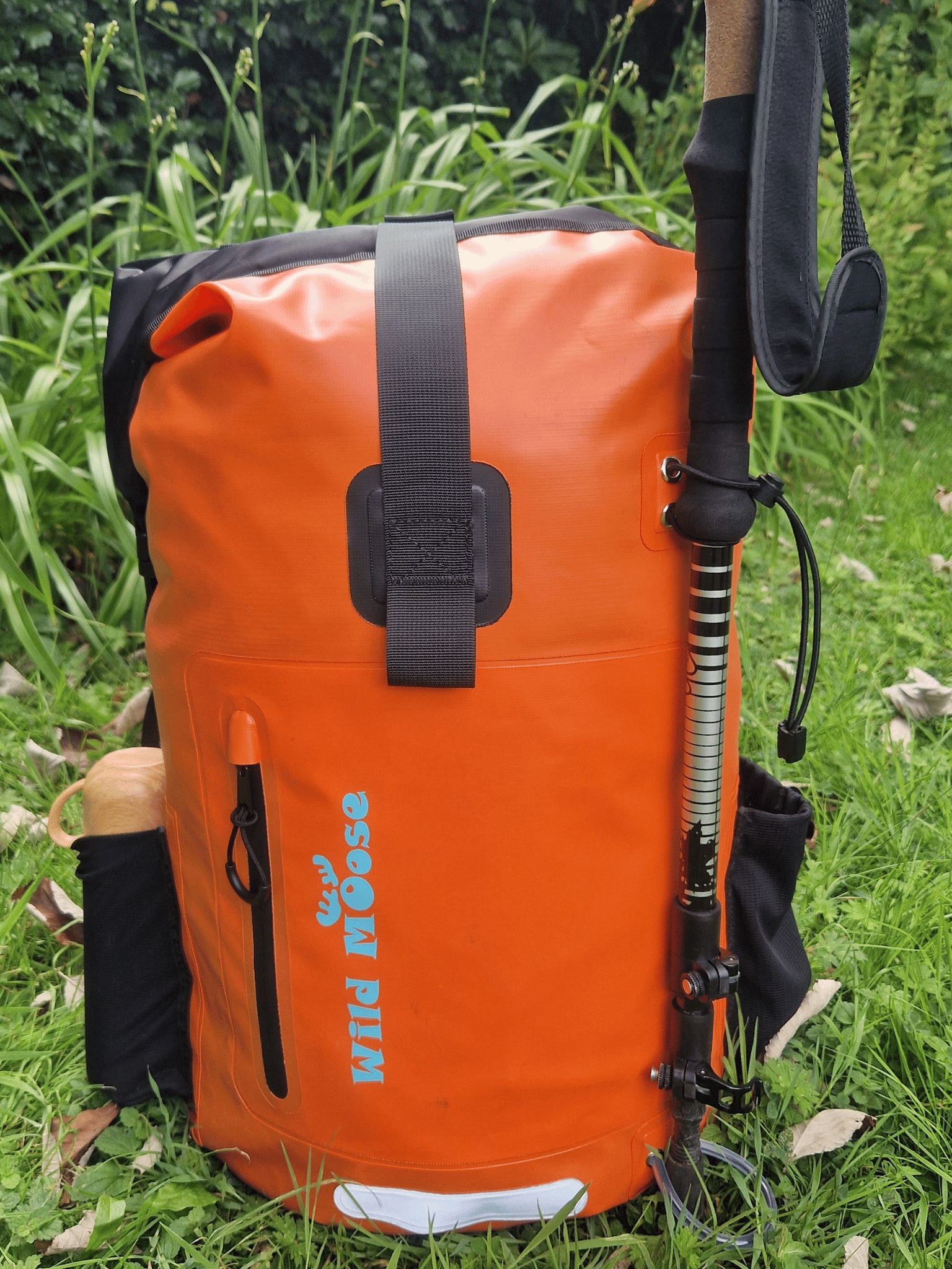 a flame orange backpack in the grass. a flask in the side pocket and a walking pole attached to the fornt