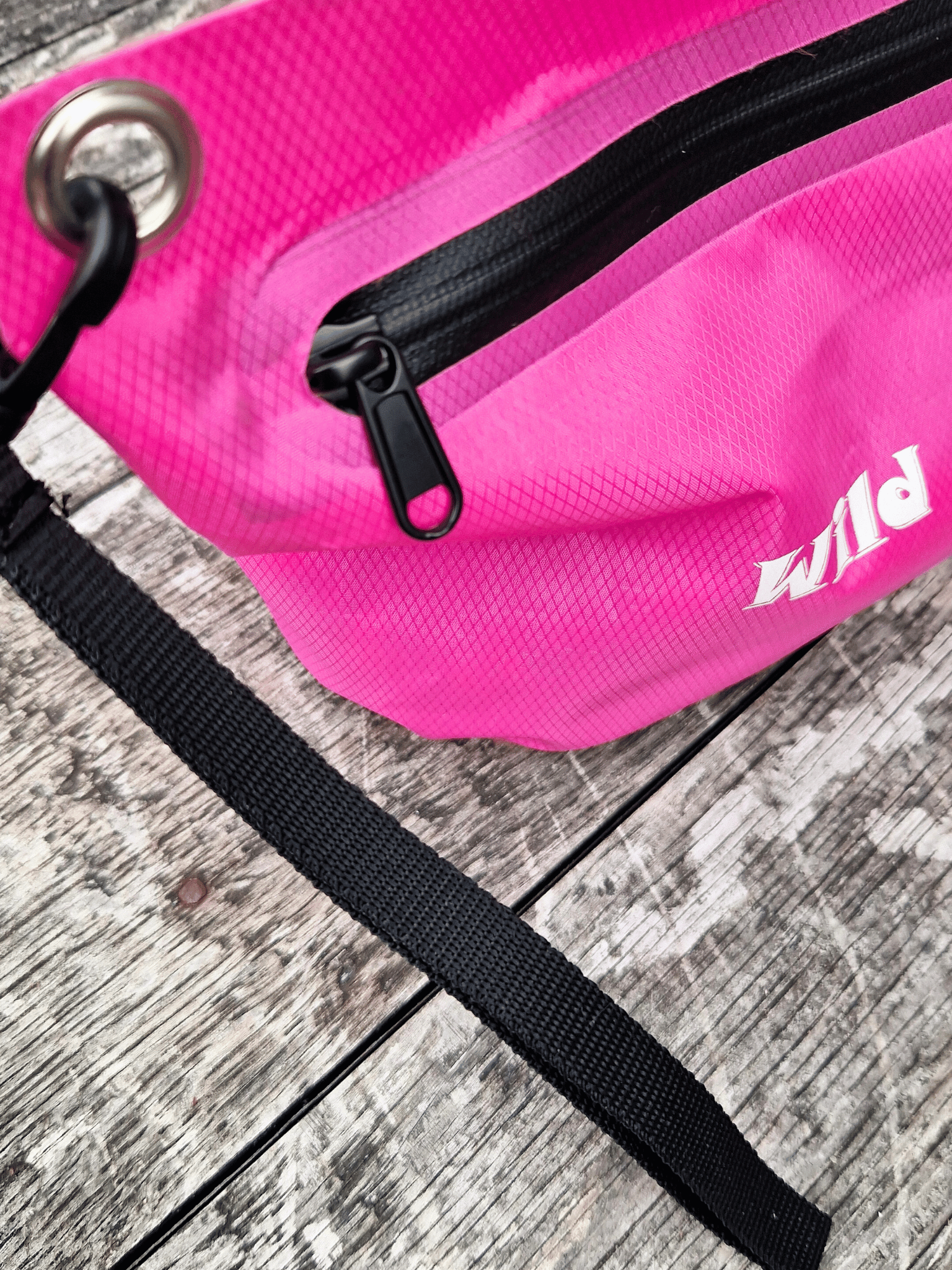 Pink zip bag with black wrist strap and 'Wild Moose' branding on a wooden surface