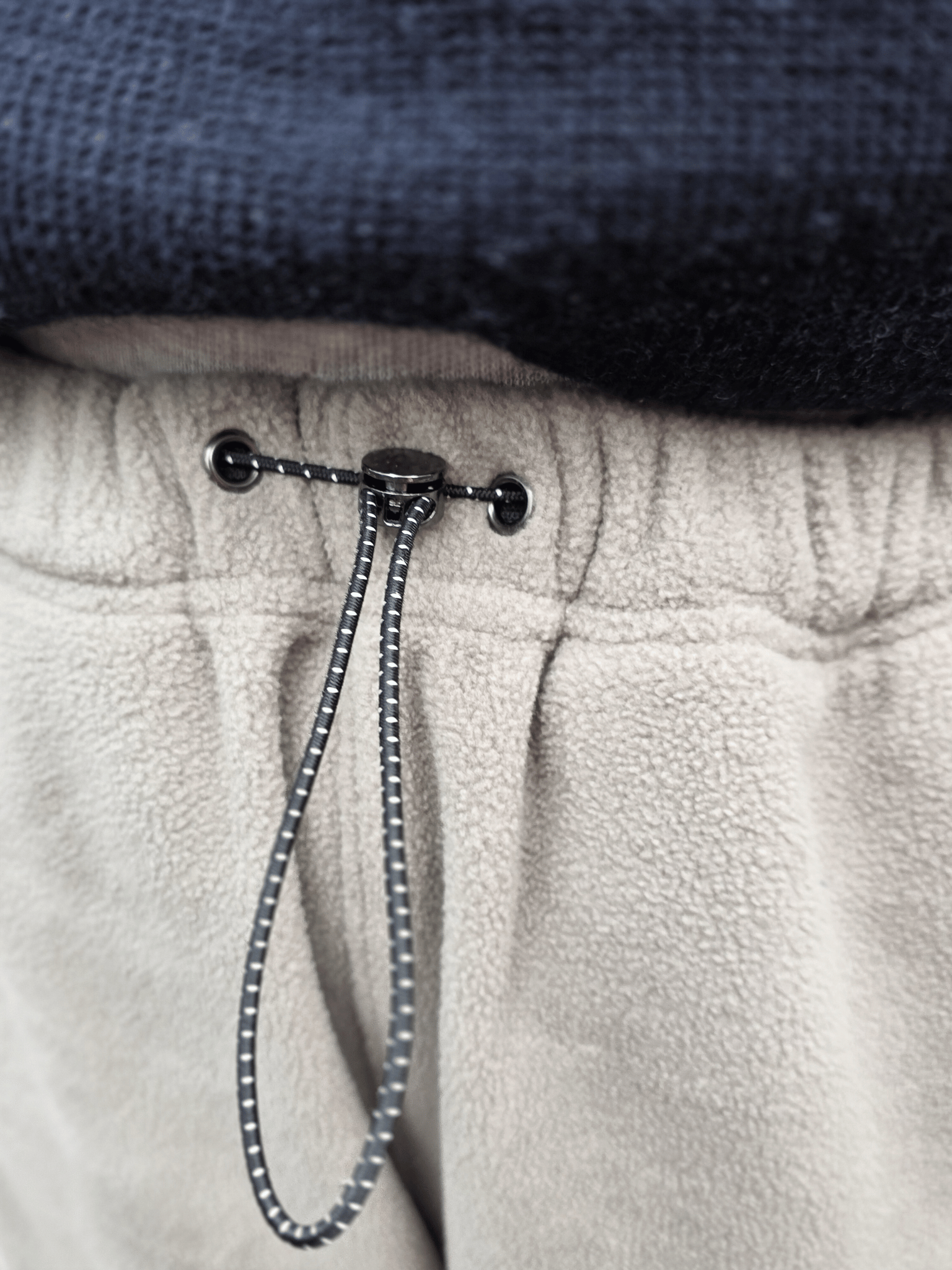 Close-up of a drawstring on beige fleece jogging pants with a dark top.