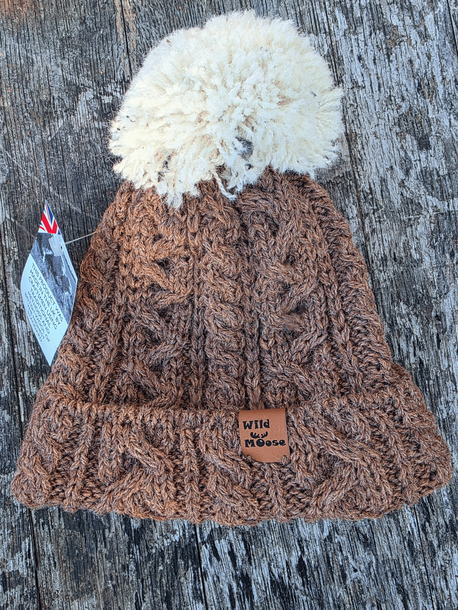 Brown knitted beanie with a white pom-pom on a wooden surface