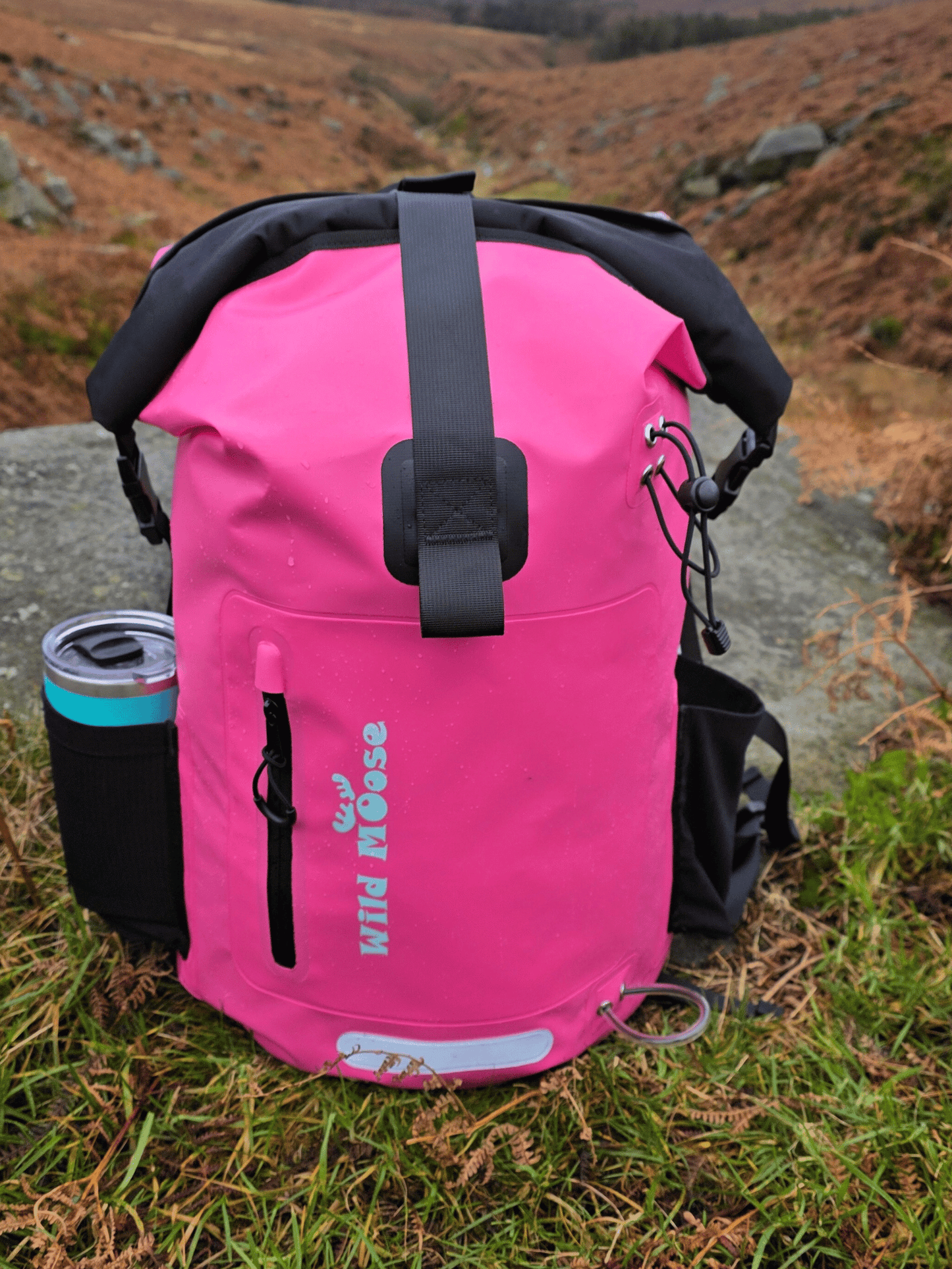 Pink dry bag with black straps on a grassy outdoor surface