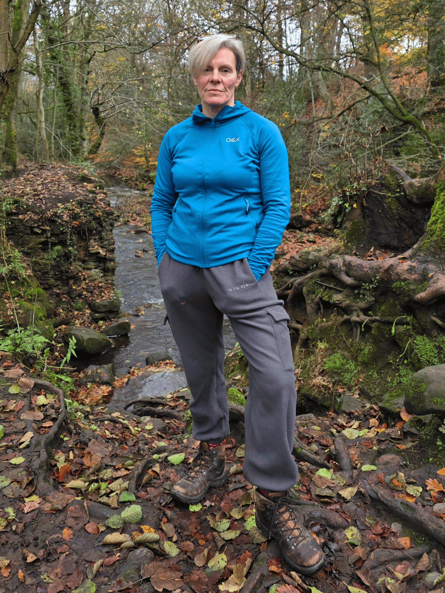 Person wearing  grey fleece jogging pants standing in a forest with a stream.