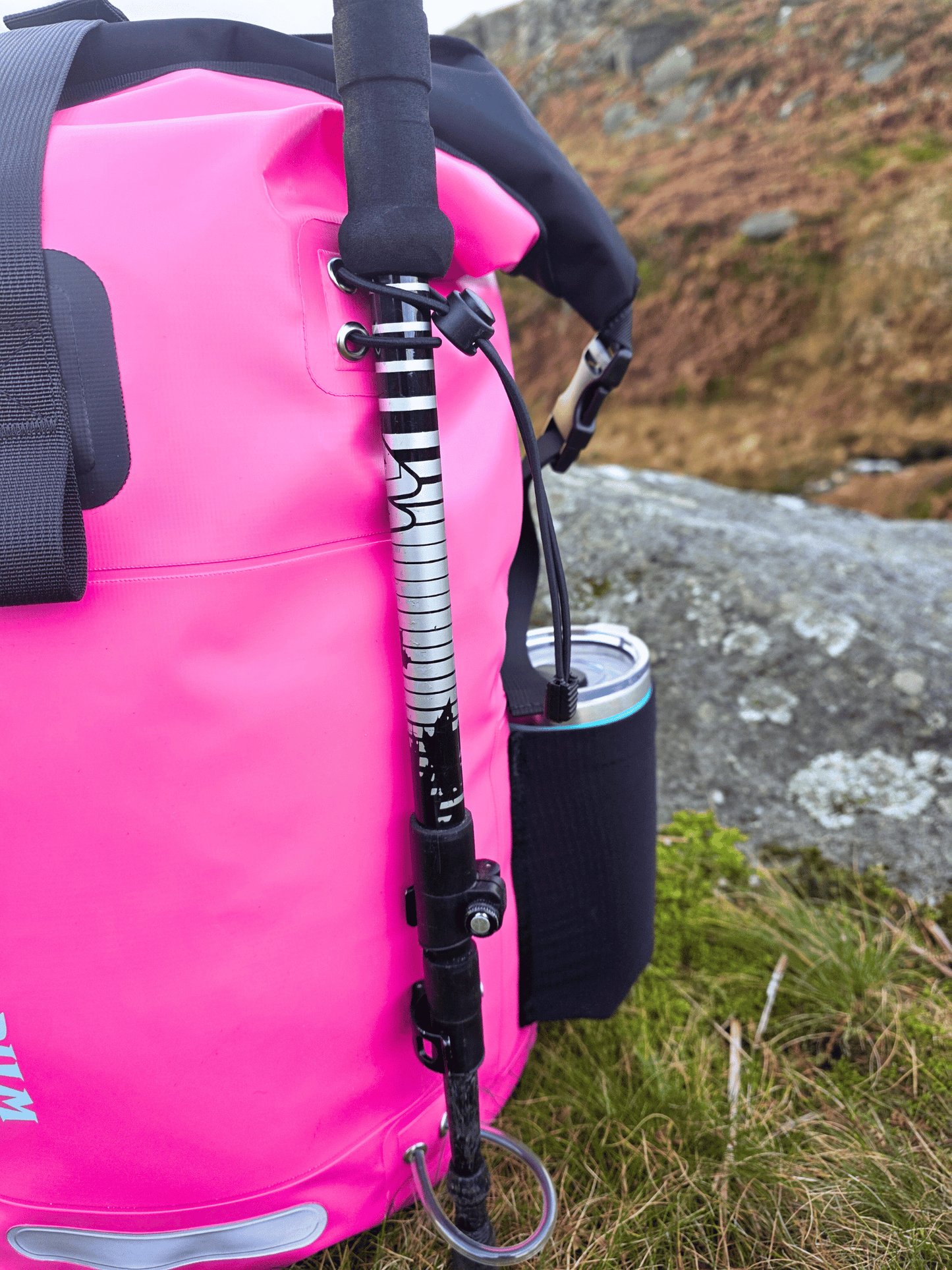 Pink dry bag with a backpack strap and a cup holding side pocket, outdoors.