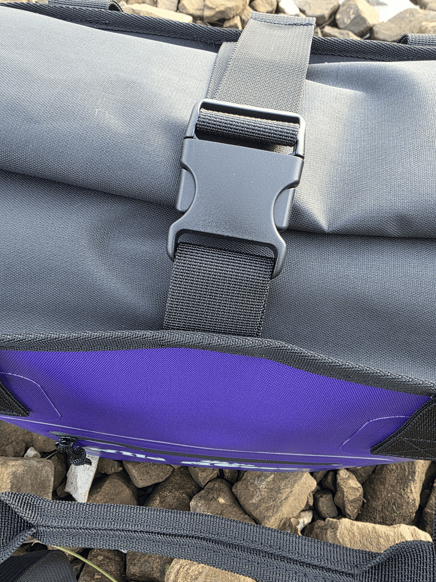 Purple tote bag with a buckle over the top on a rocky beach